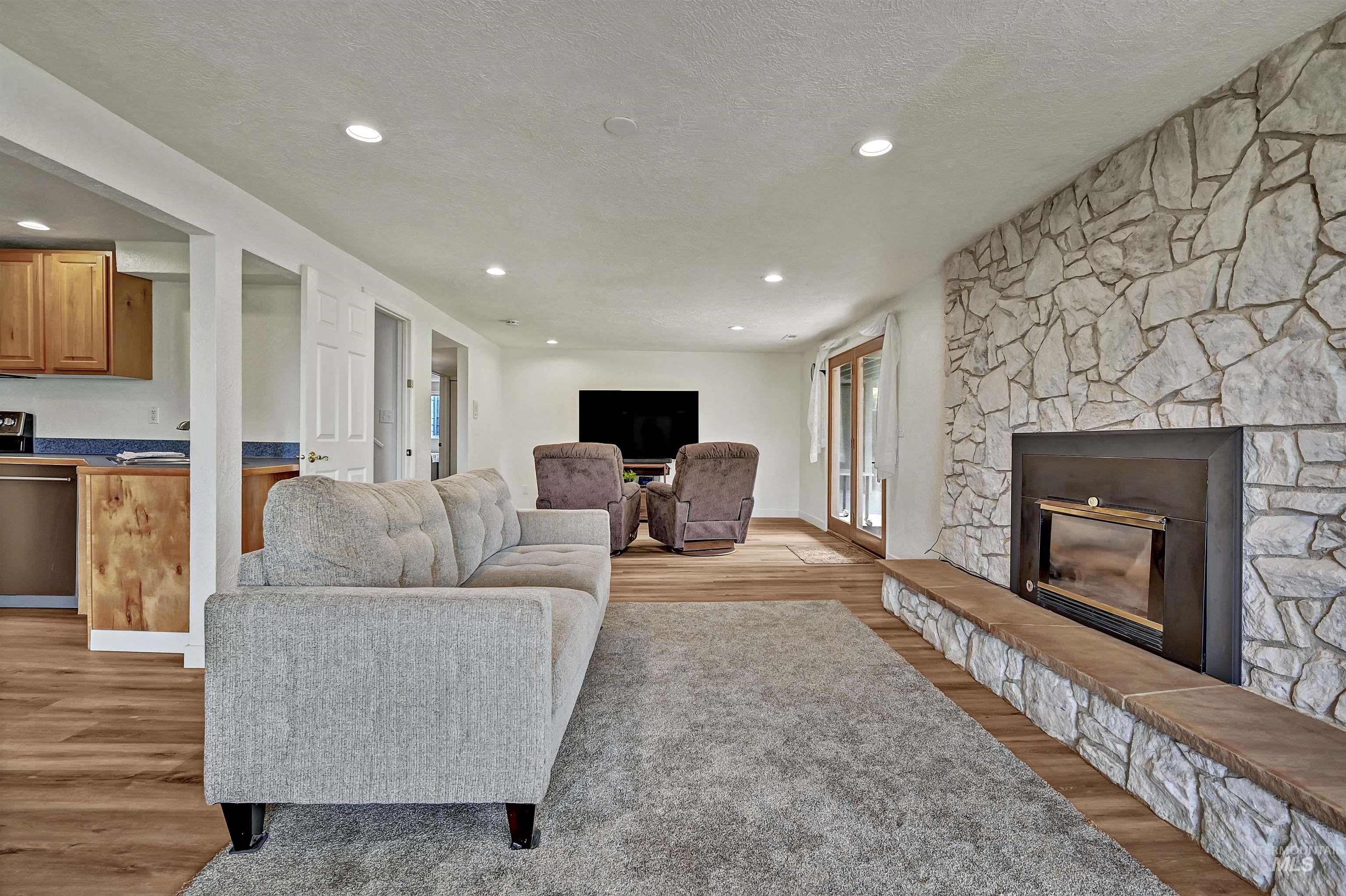 Living room featuring light wood-style flooring, a stone fireplace, recessed lighting, and a textured ceiling