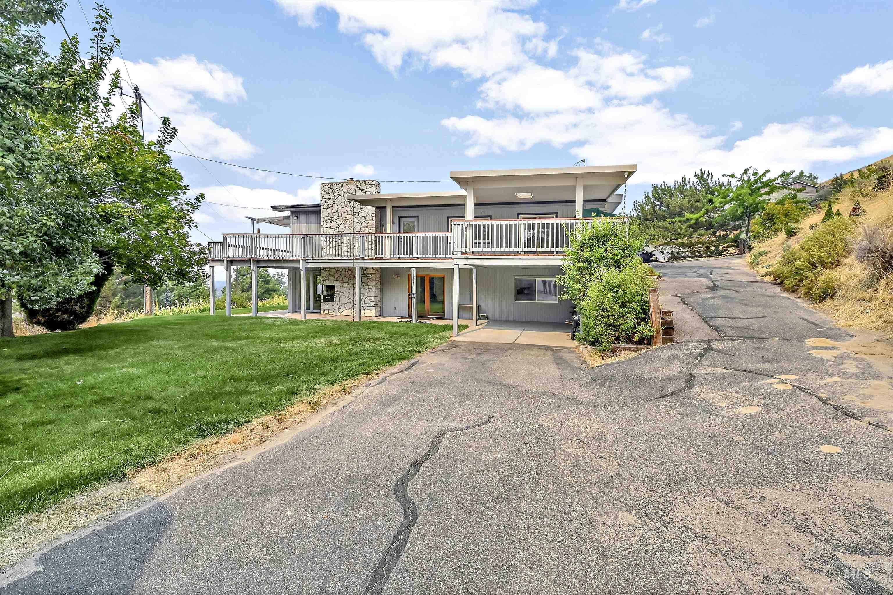 View of front of house featuring a front lawn, asphalt driveway, stone siding, and a balcony
