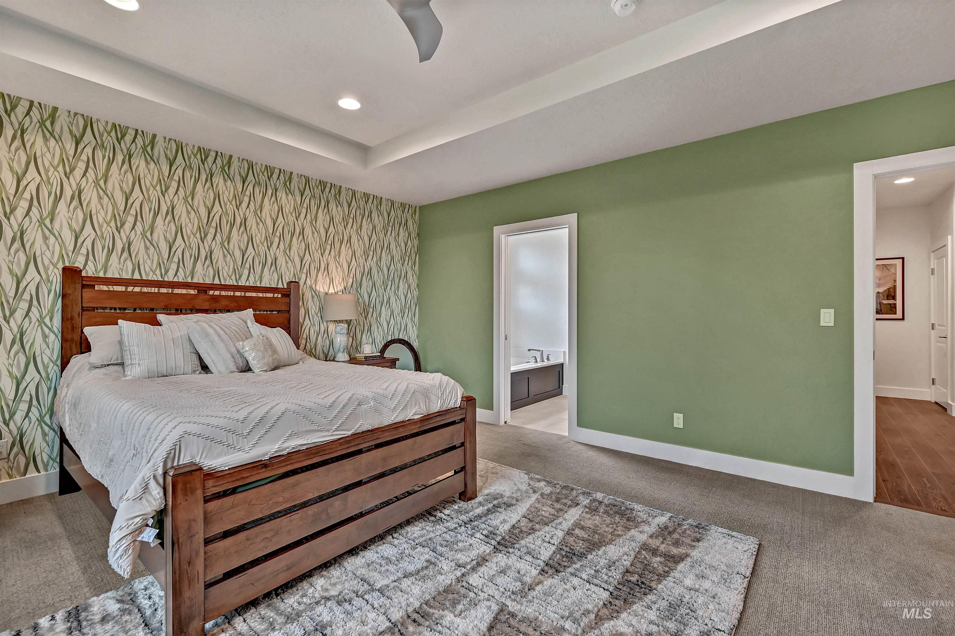 Carpeted bedroom with an accent wall, ensuite bathroom, a tray ceiling, recessed lighting, and wallpapered walls