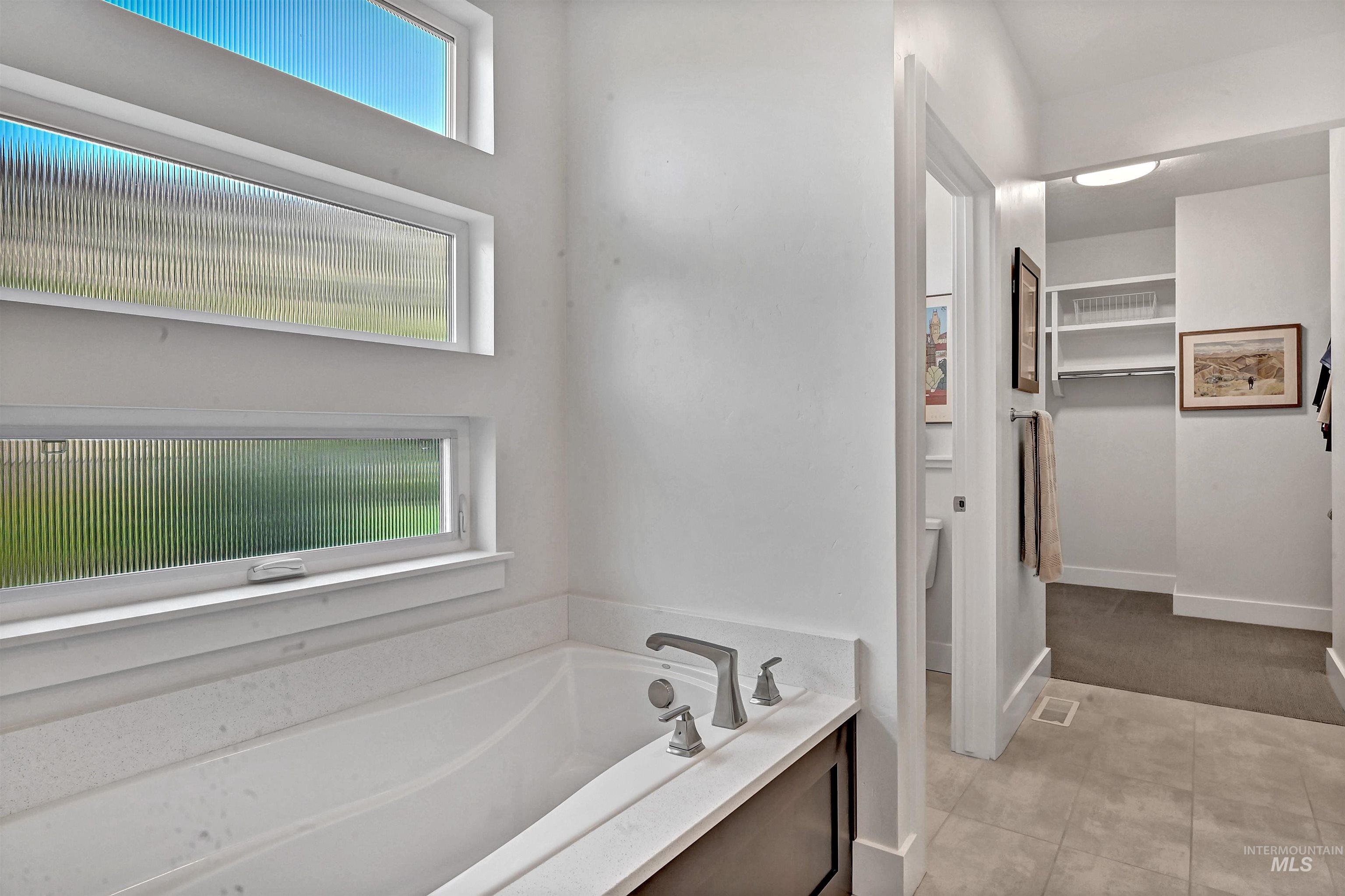 Bathroom with a spacious closet, a garden tub, and light tile patterned floors