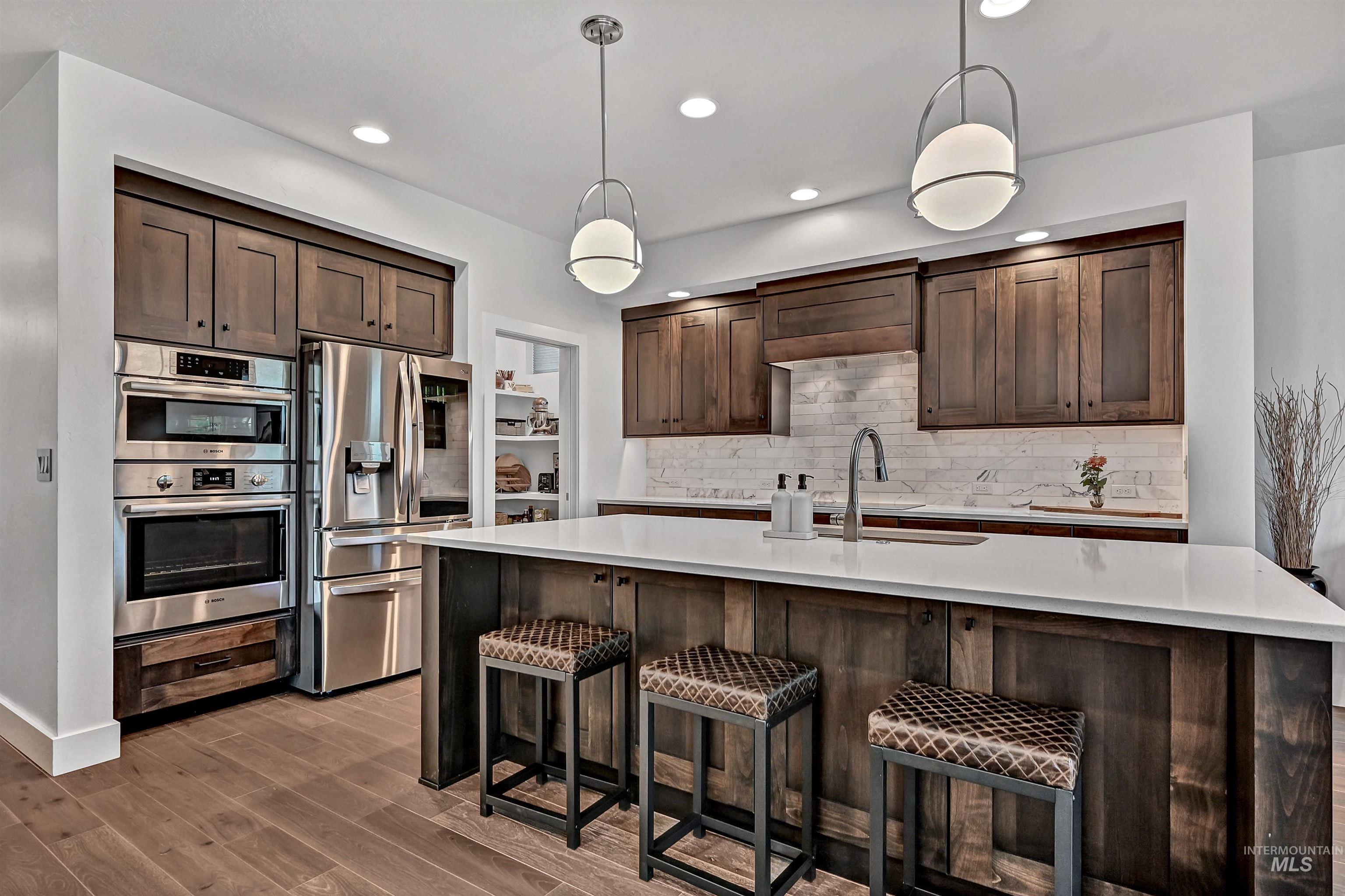Kitchen featuring dark brown cabinets, hanging light fixtures, stainless steel appliances, tasteful backsplash, and recessed lighting