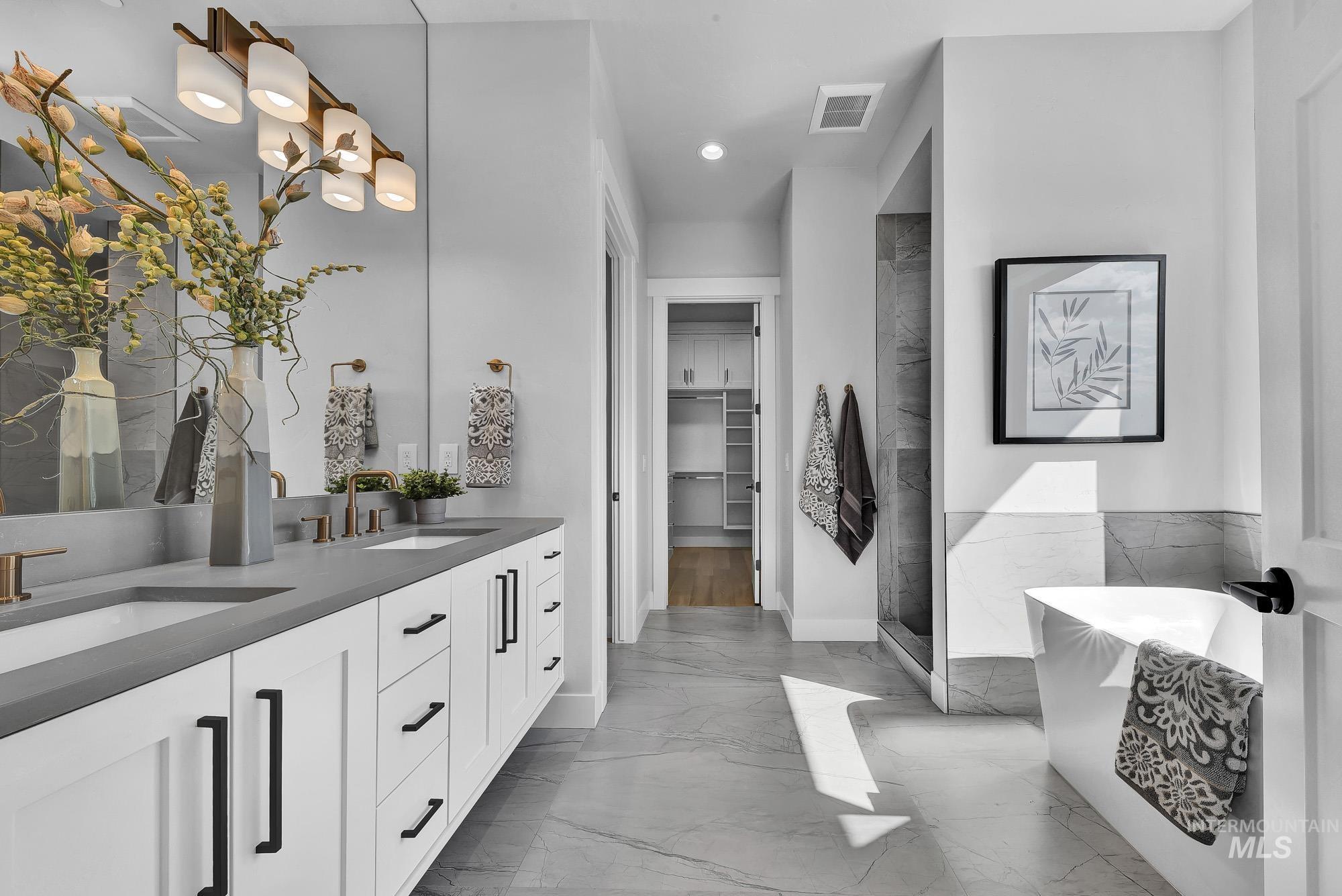 Full bathroom with double vanity, a spacious closet, a soaking tub, a stall shower, and light marble finish floors