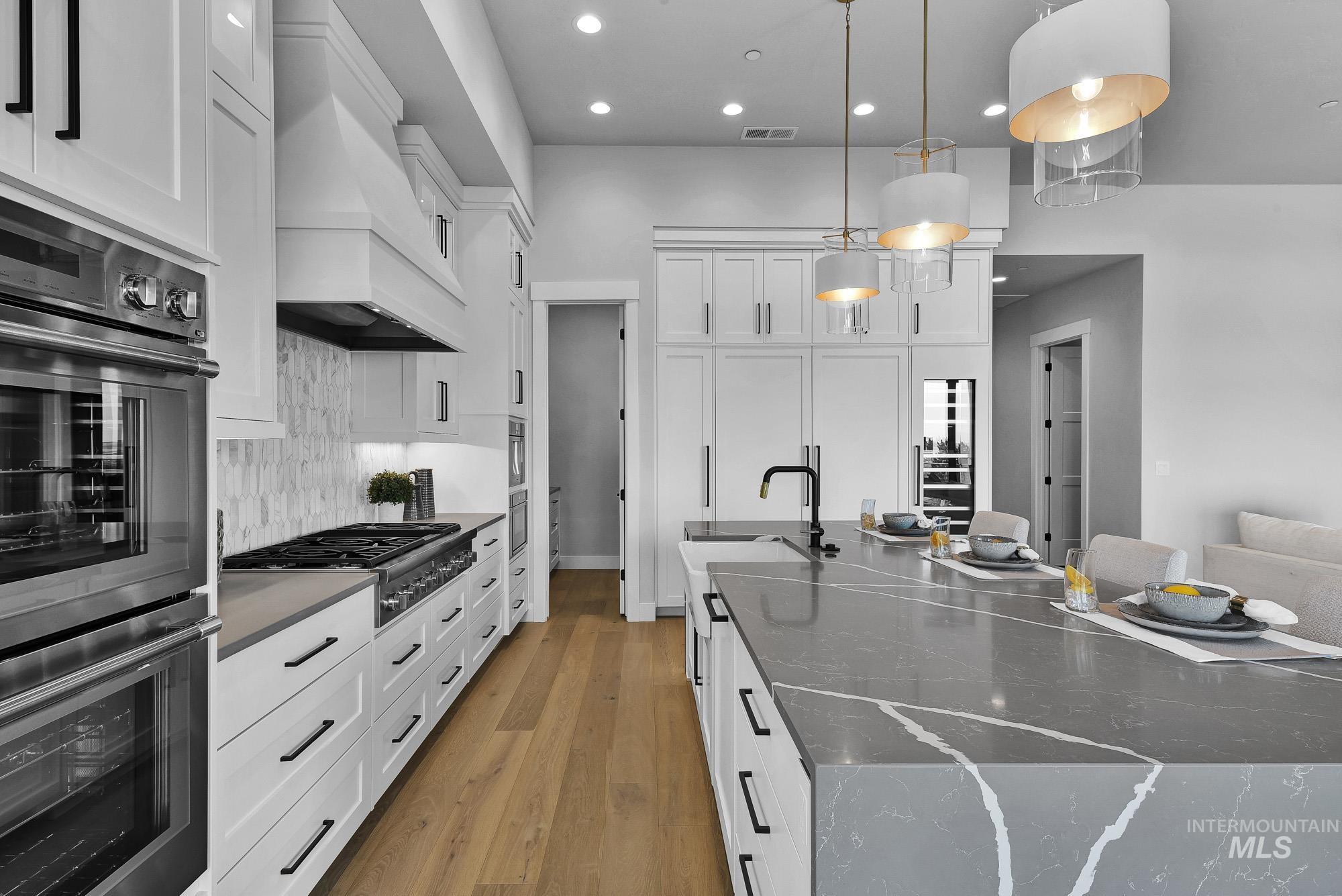 Kitchen with stainless steel appliances, decorative light fixtures, light wood-style floors, dark stone counters, and white cabinetry