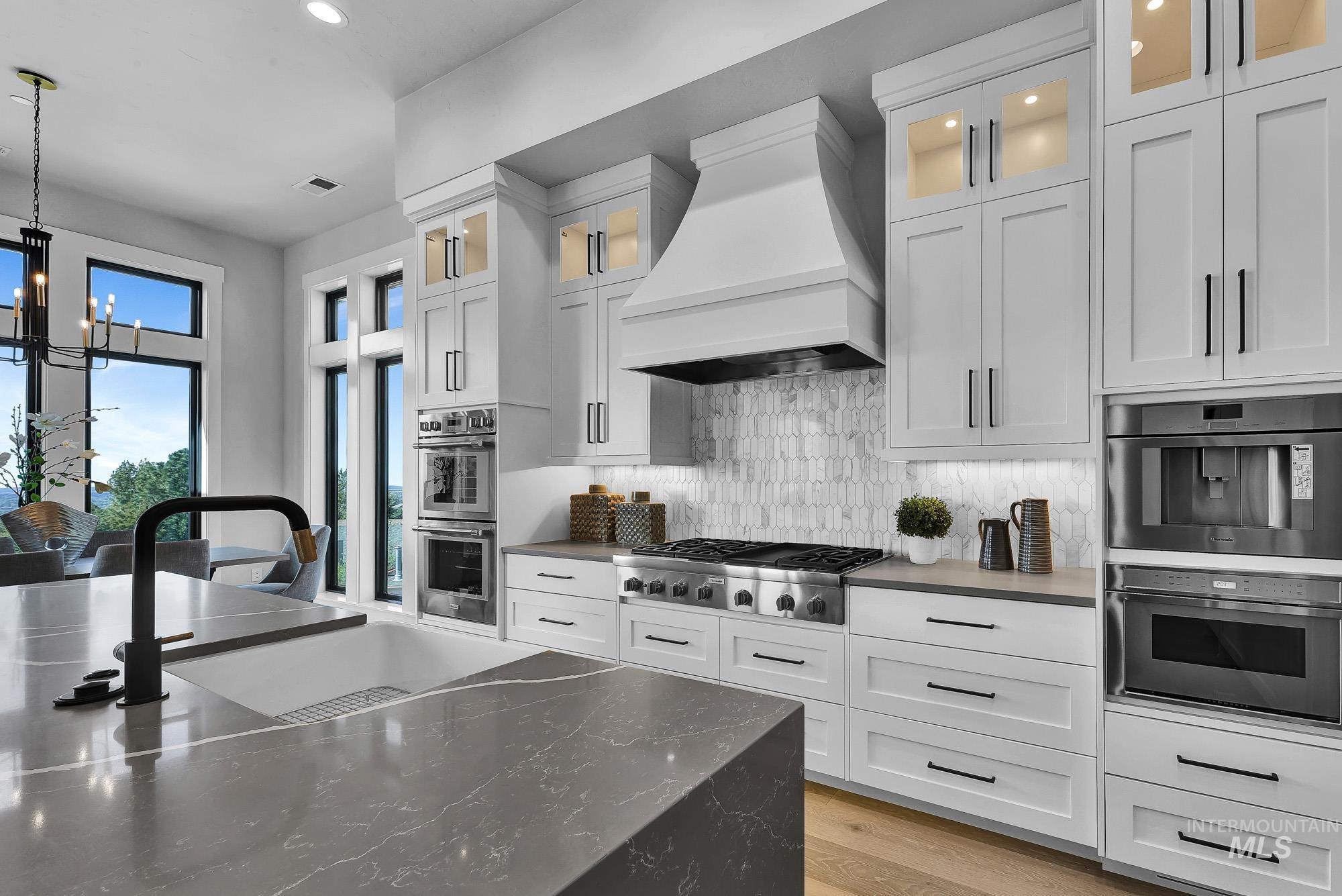 Kitchen featuring pendant lighting, glass insert cabinets, a chandelier, custom range hood, and recessed lighting