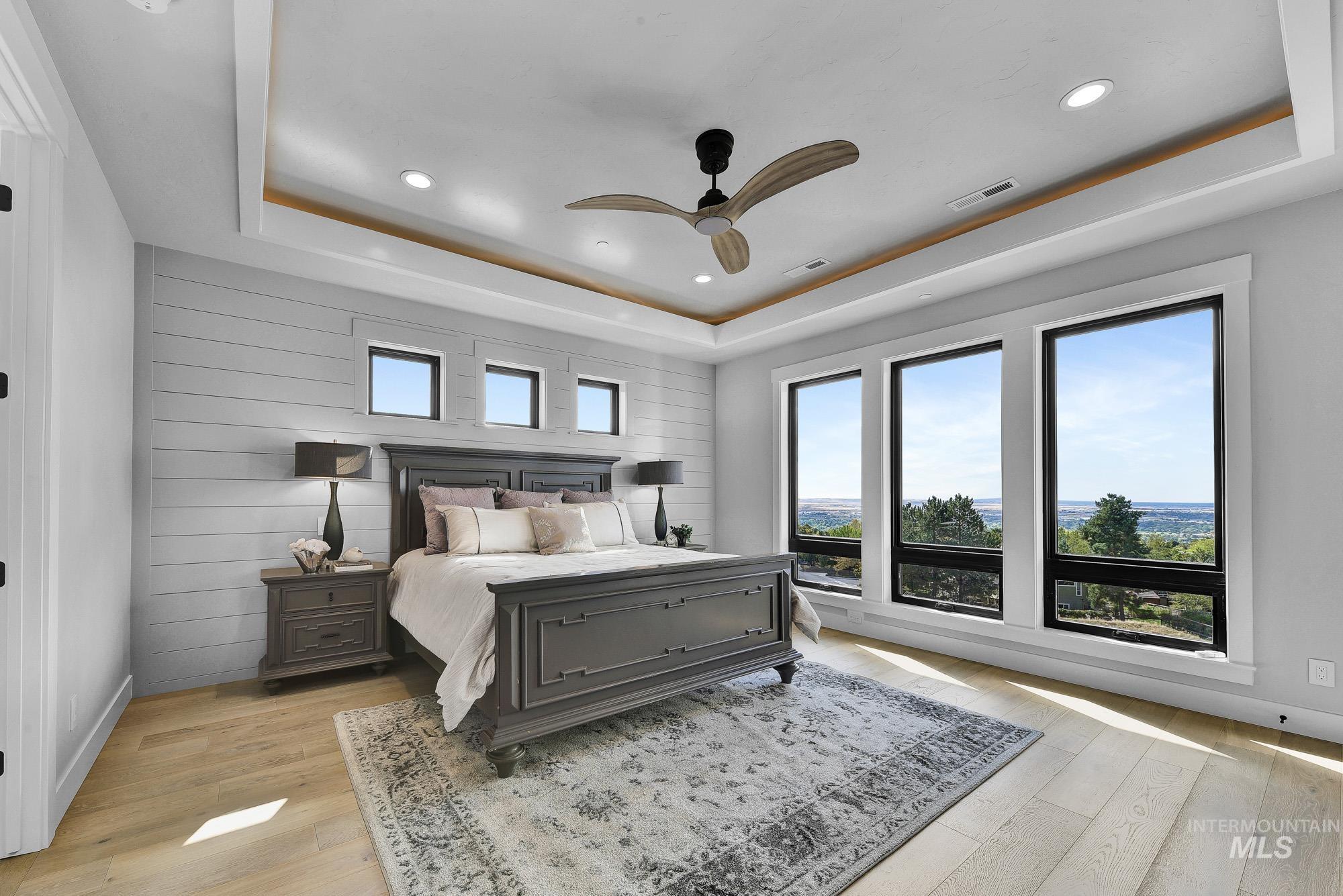 Bedroom with a tray ceiling, light wood finished floors, recessed lighting, ceiling fan, and wood walls