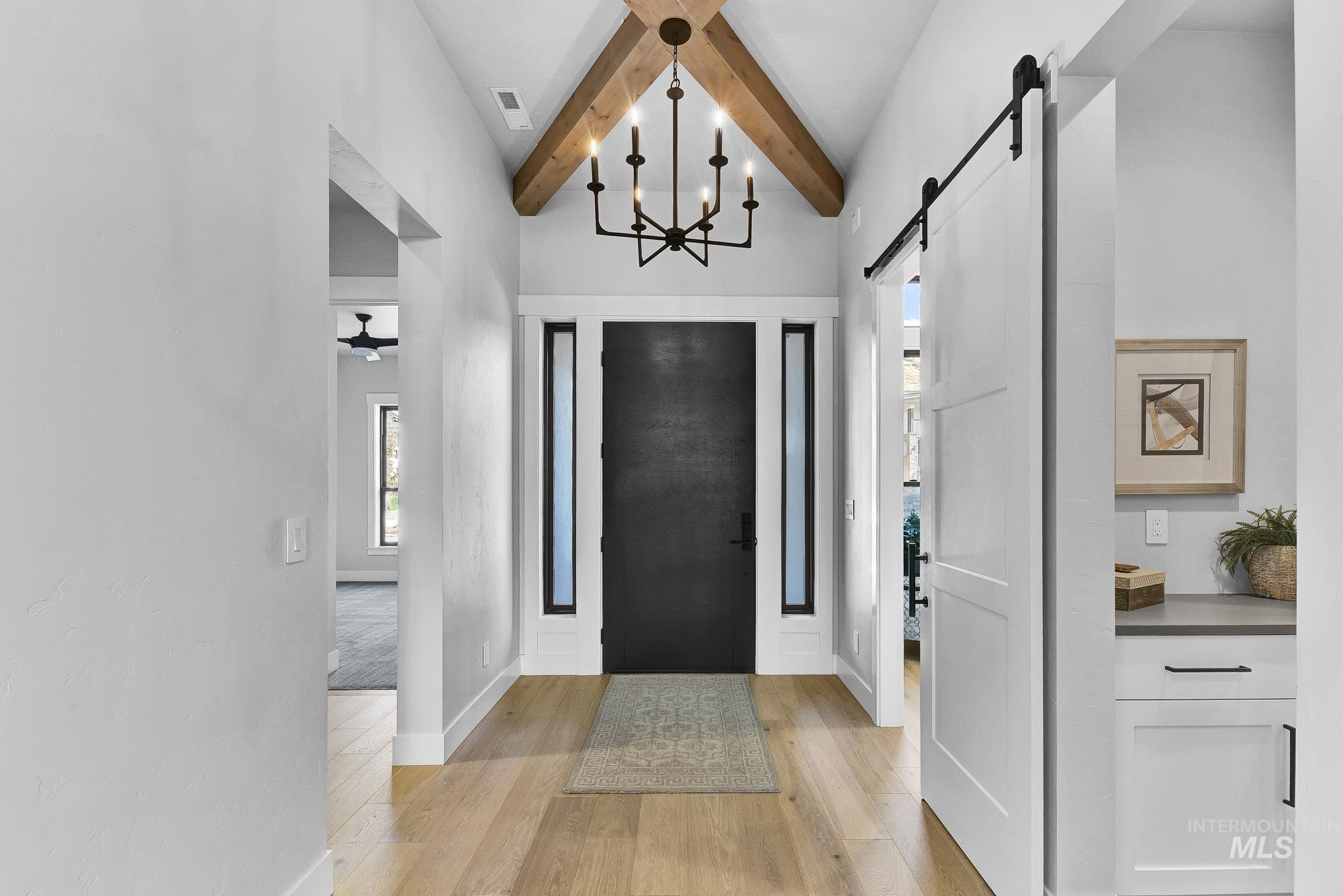Entrance foyer with light wood finished floors, a chandelier, a barn door, and beam ceiling