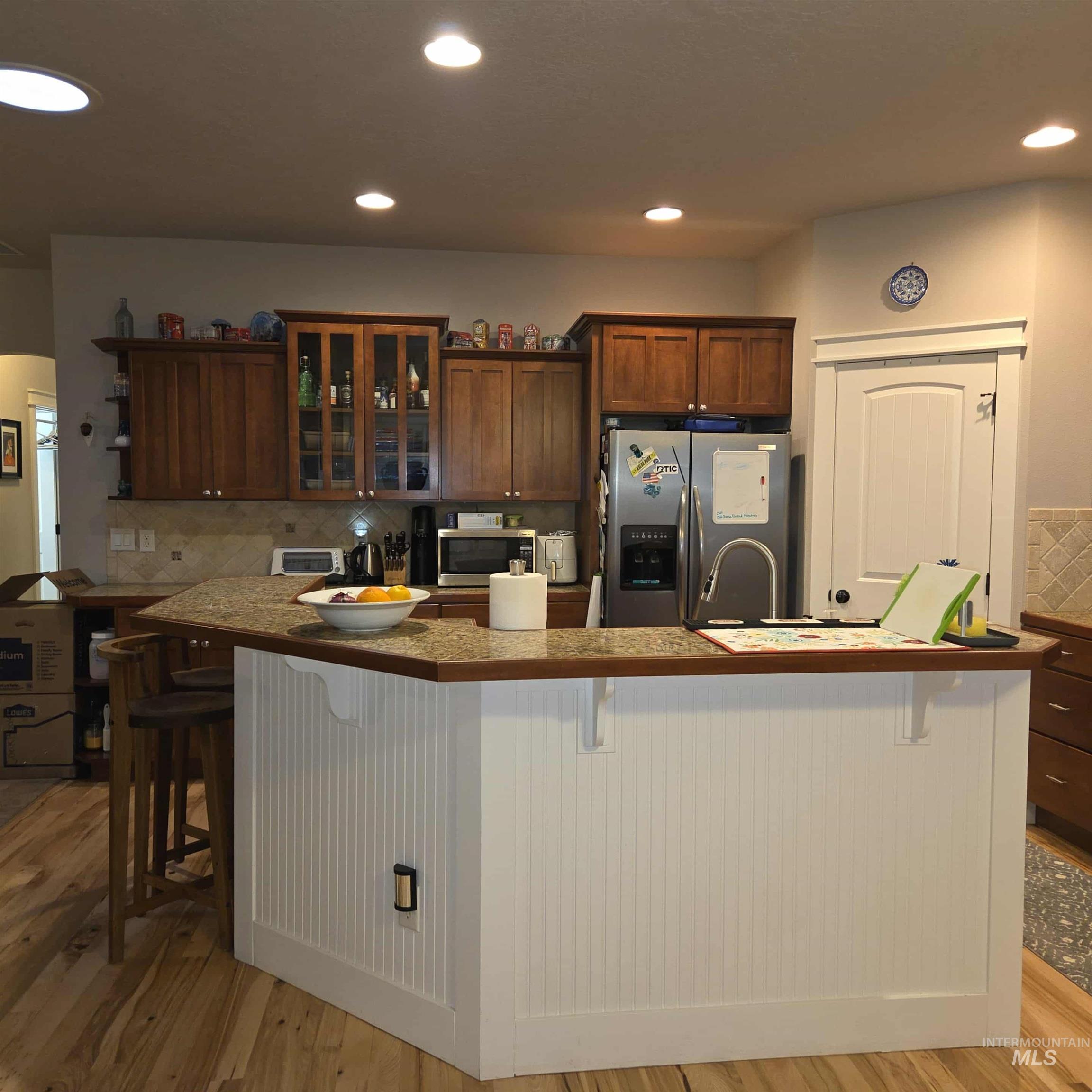 Kitchen featuring backsplash, a kitchen bar, glass insert cabinets, recessed lighting, and appliances with stainless steel finishes