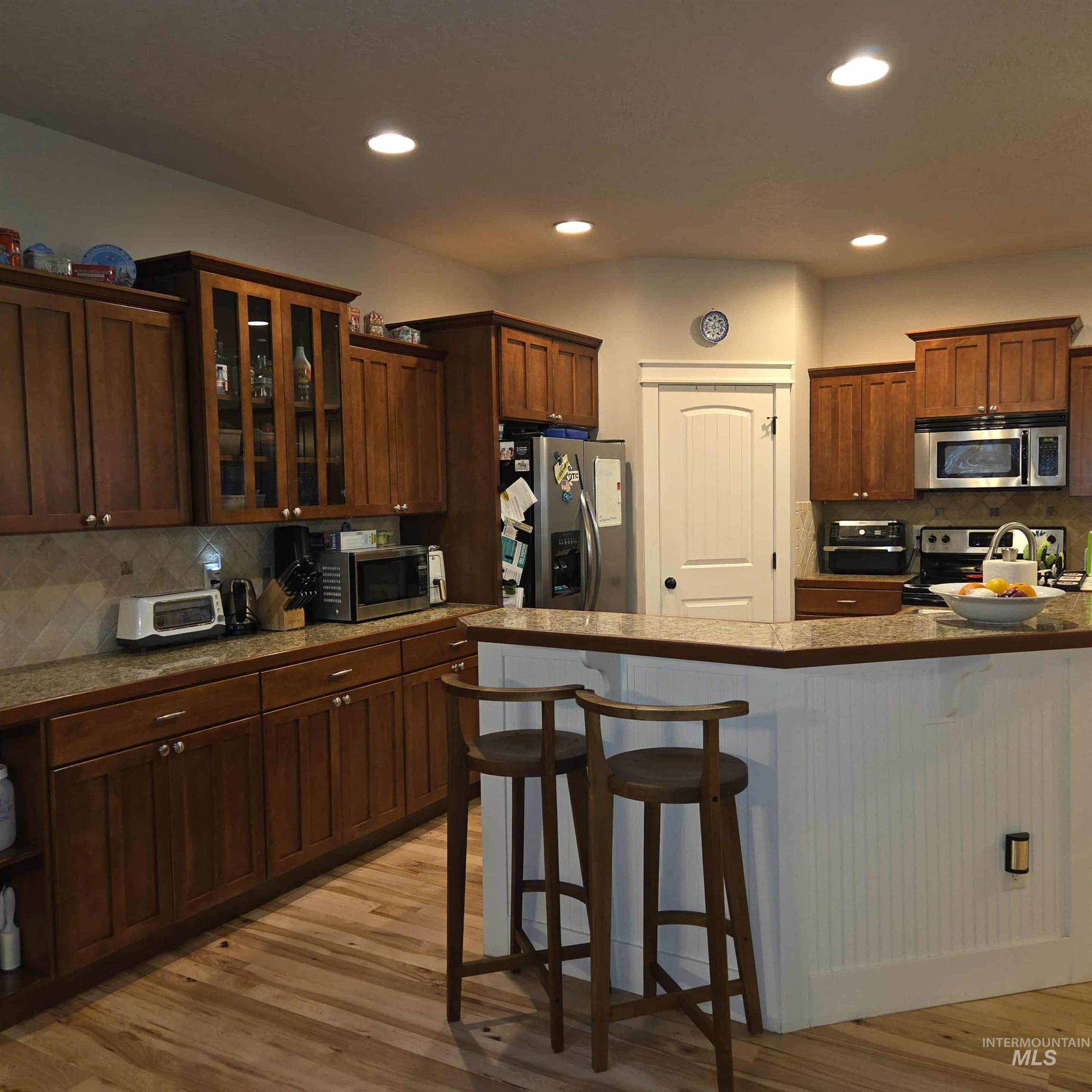 Kitchen with tasteful backsplash, a kitchen bar, stainless steel appliances, recessed lighting, and light wood-style floors