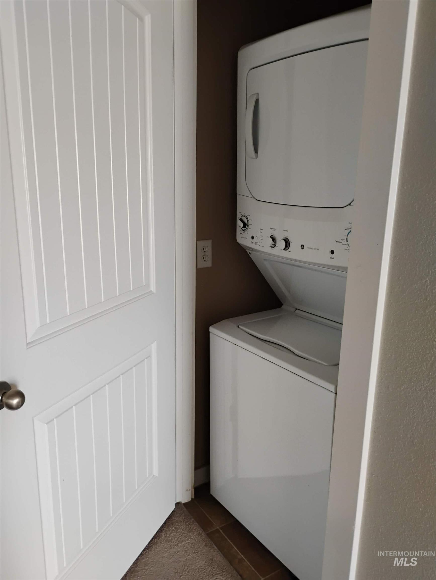 Washroom with dark tile patterned floors and stacked washer and clothes dryer