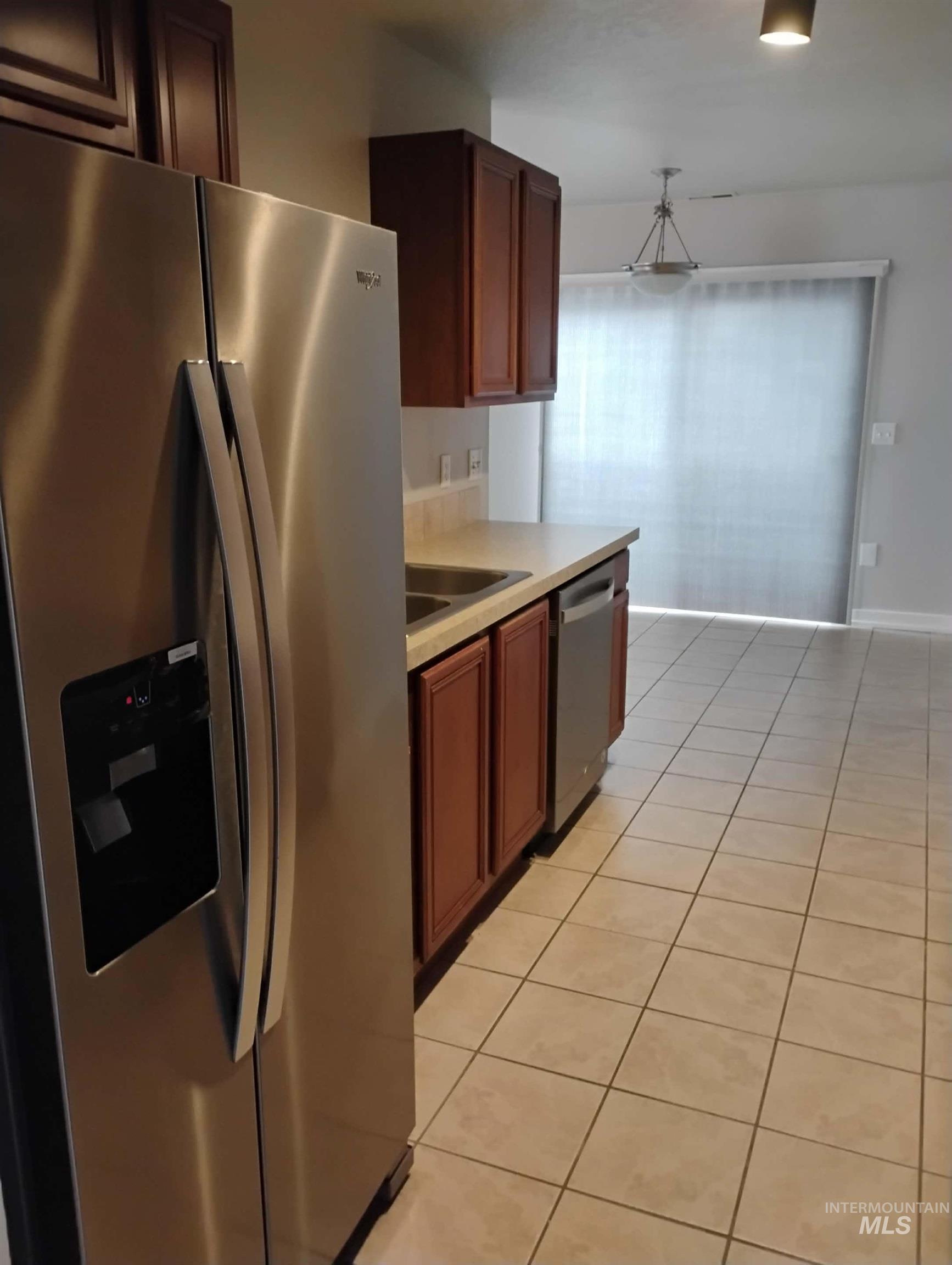 Kitchen with stainless steel appliances, light countertops, light tile patterned floors, and hanging light fixtures