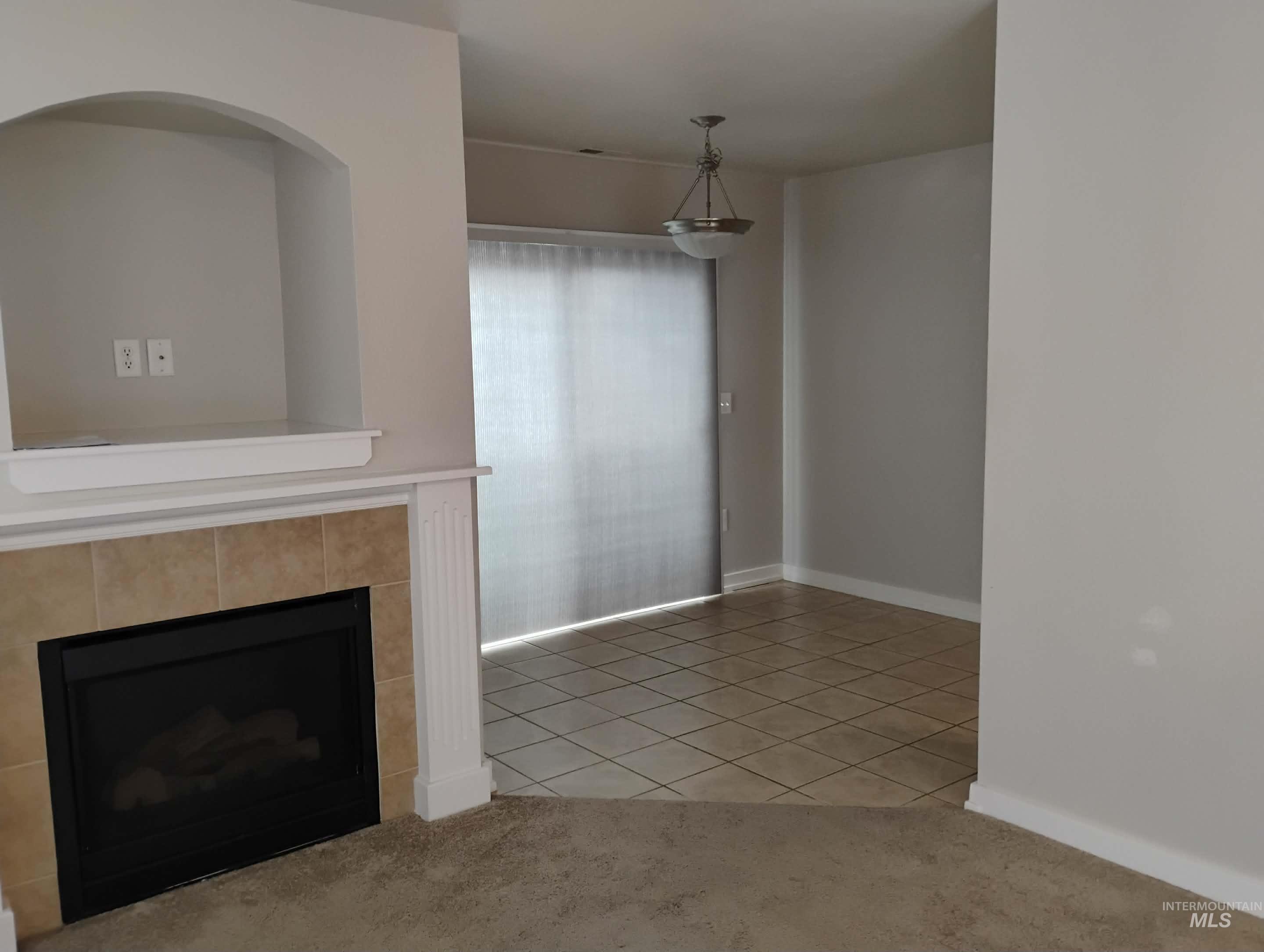 Unfurnished living room featuring light tile patterned floors, light carpet, and a tiled fireplace