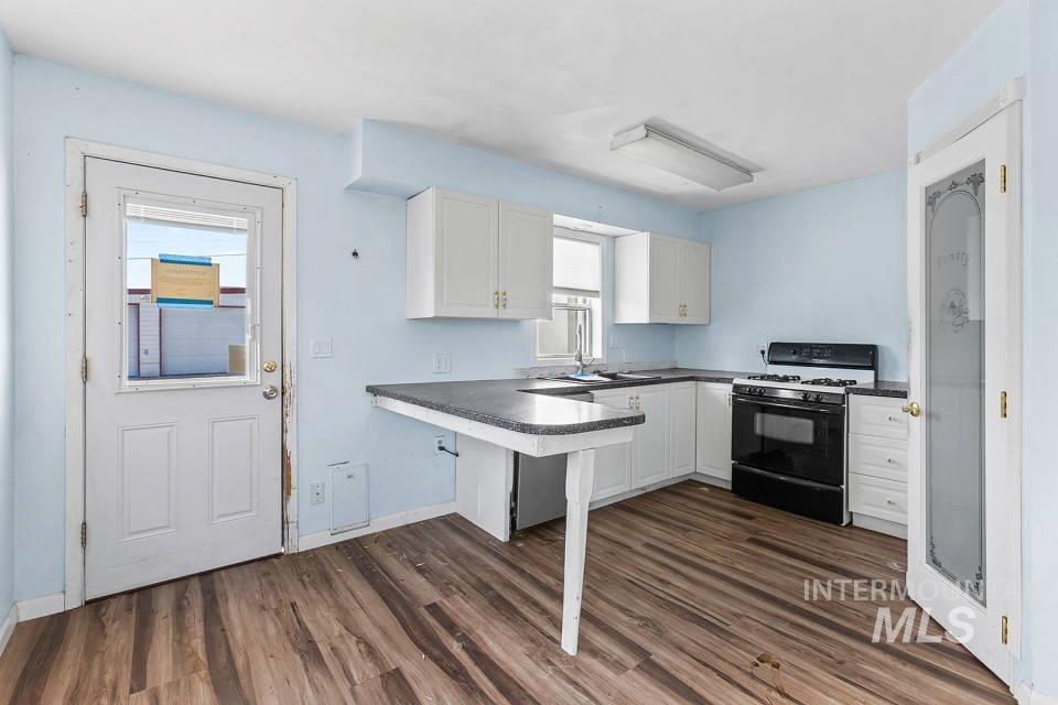 Kitchen with range with gas cooktop, white cabinetry, dark countertops, dark wood-style floors, and a peninsula