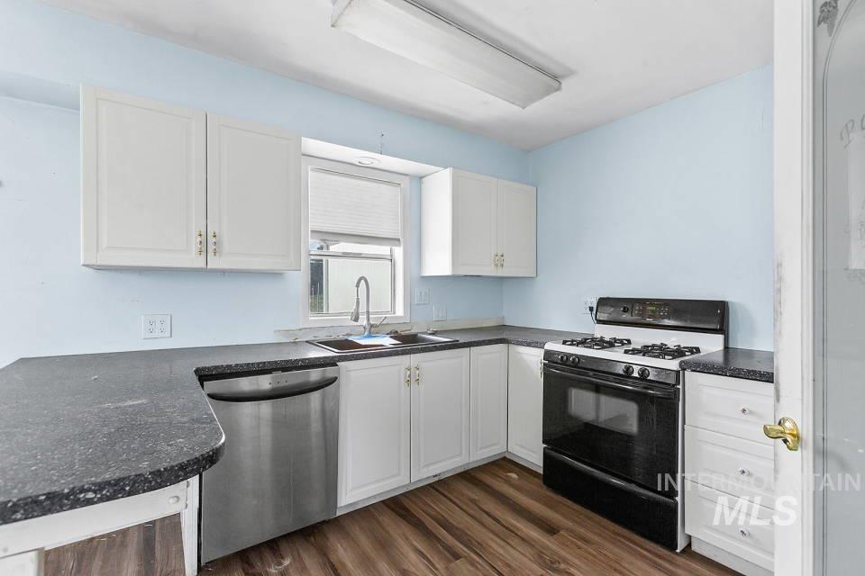 Kitchen featuring range with gas stovetop, white cabinets, stainless steel dishwasher, dark wood finished floors, and dark stone countertops