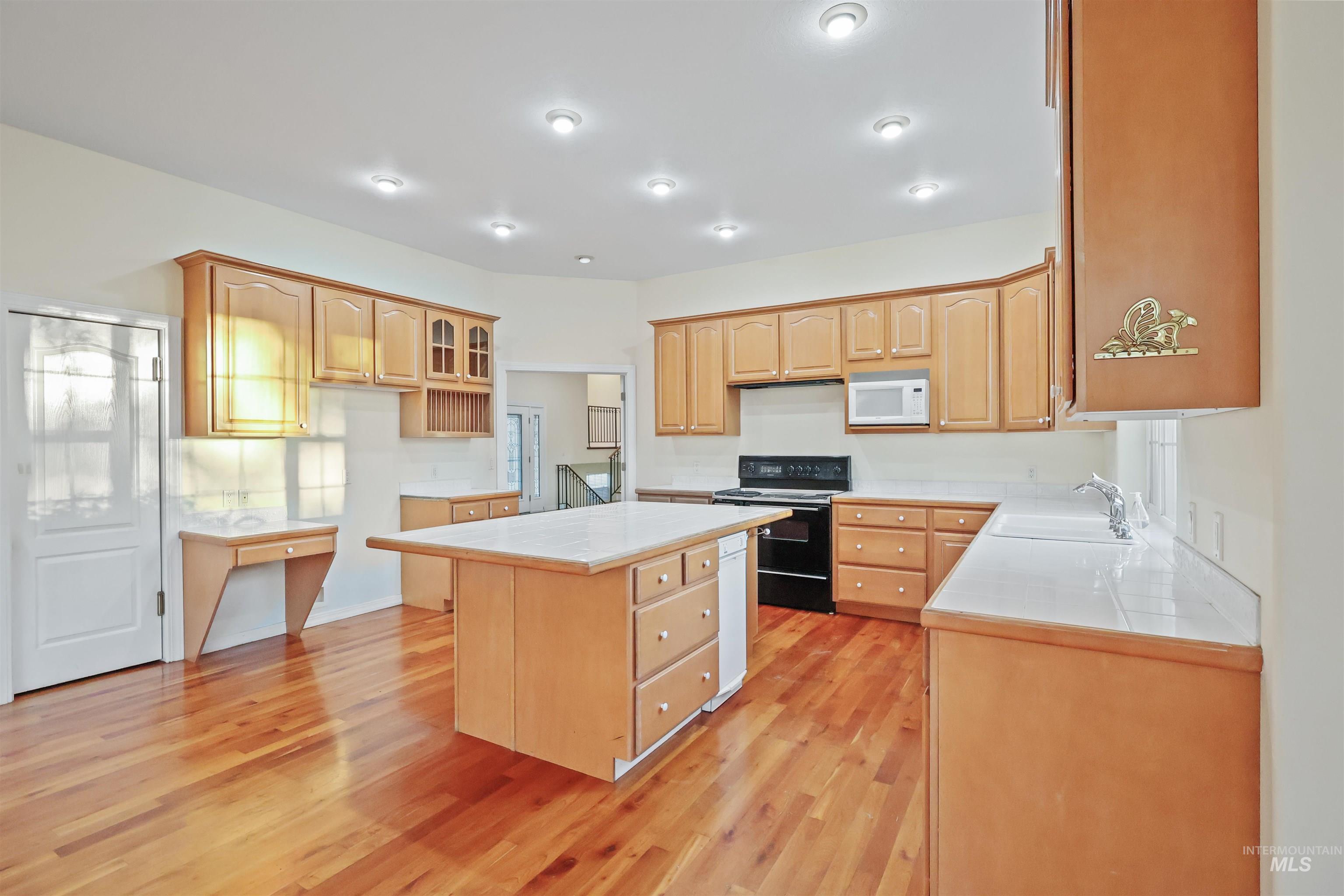 Kitchen featuring a kitchen island, black electric range oven, light wood-style flooring, white microwave, and tile counters