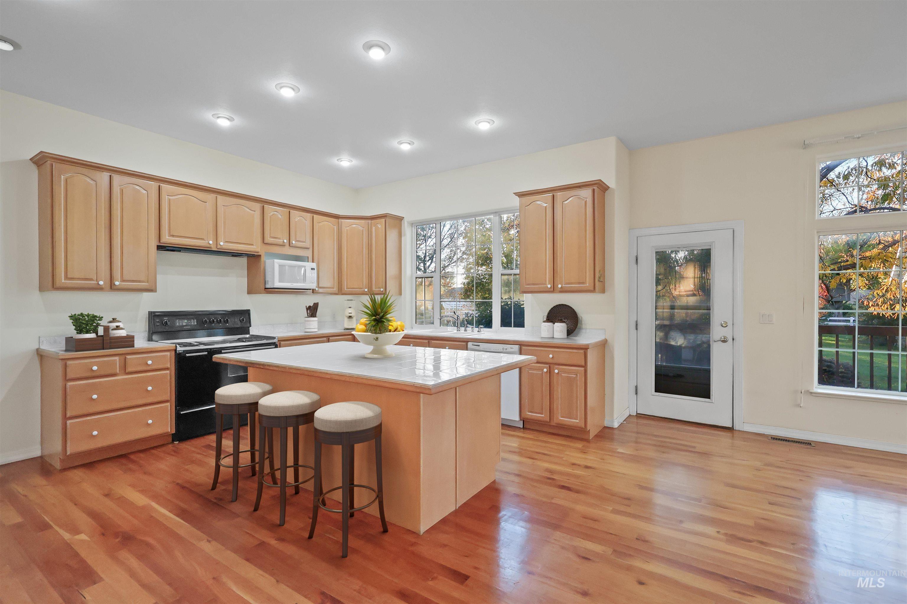 Kitchen with a kitchen bar, white appliances, a center island, light countertops, and light brown cabinetry