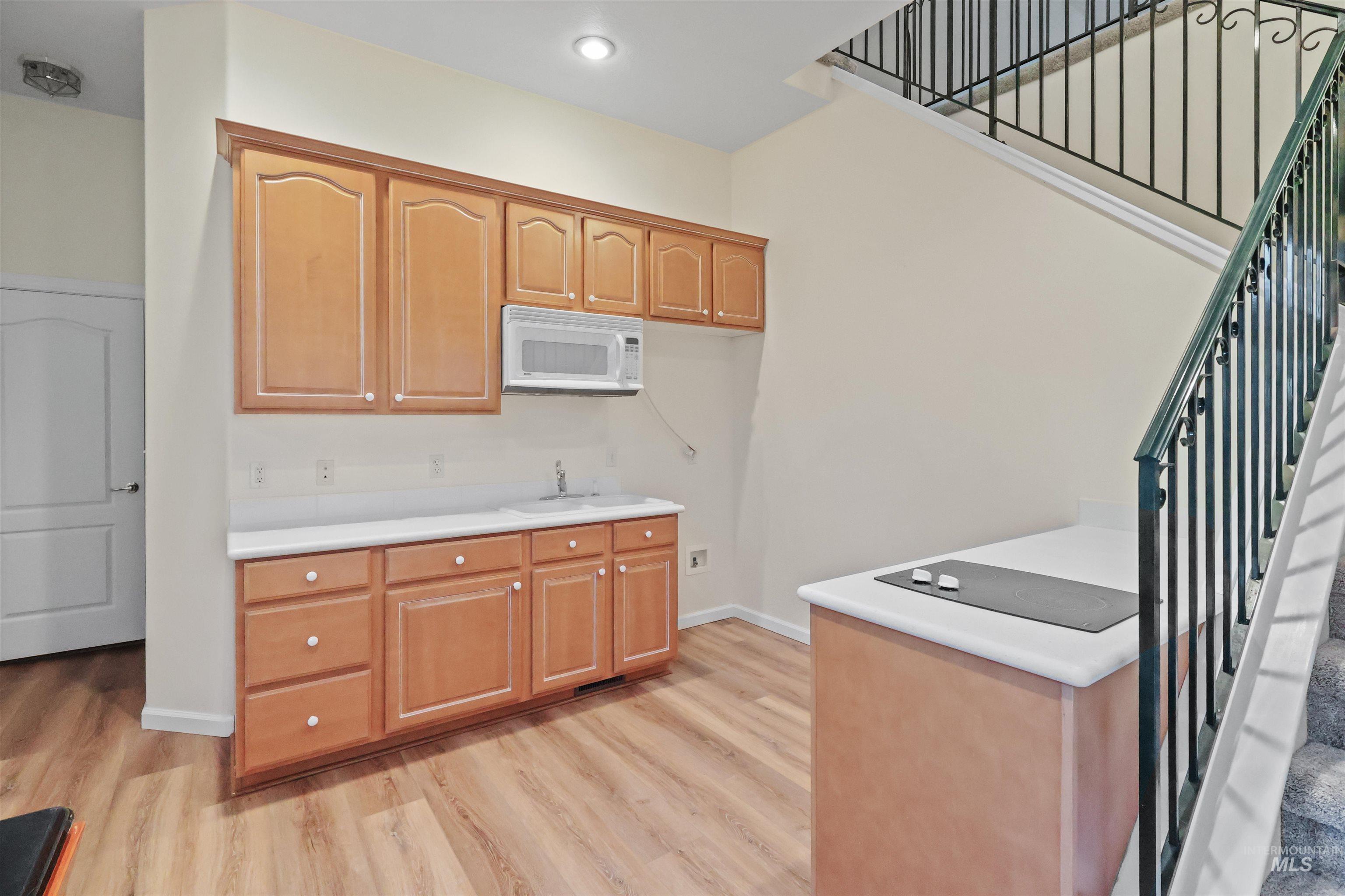 Kitchen with light countertops, white microwave, light wood-type flooring, and recessed lighting