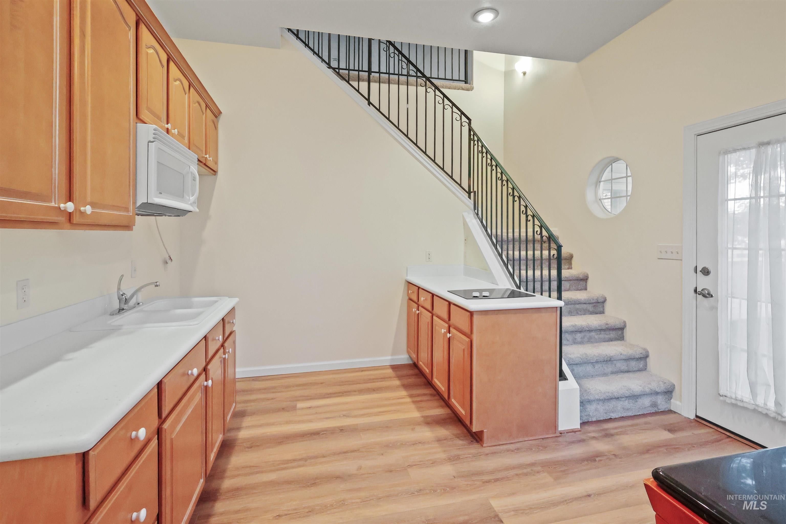 Kitchen with light wood finished floors, white microwave, and brown cabinetry