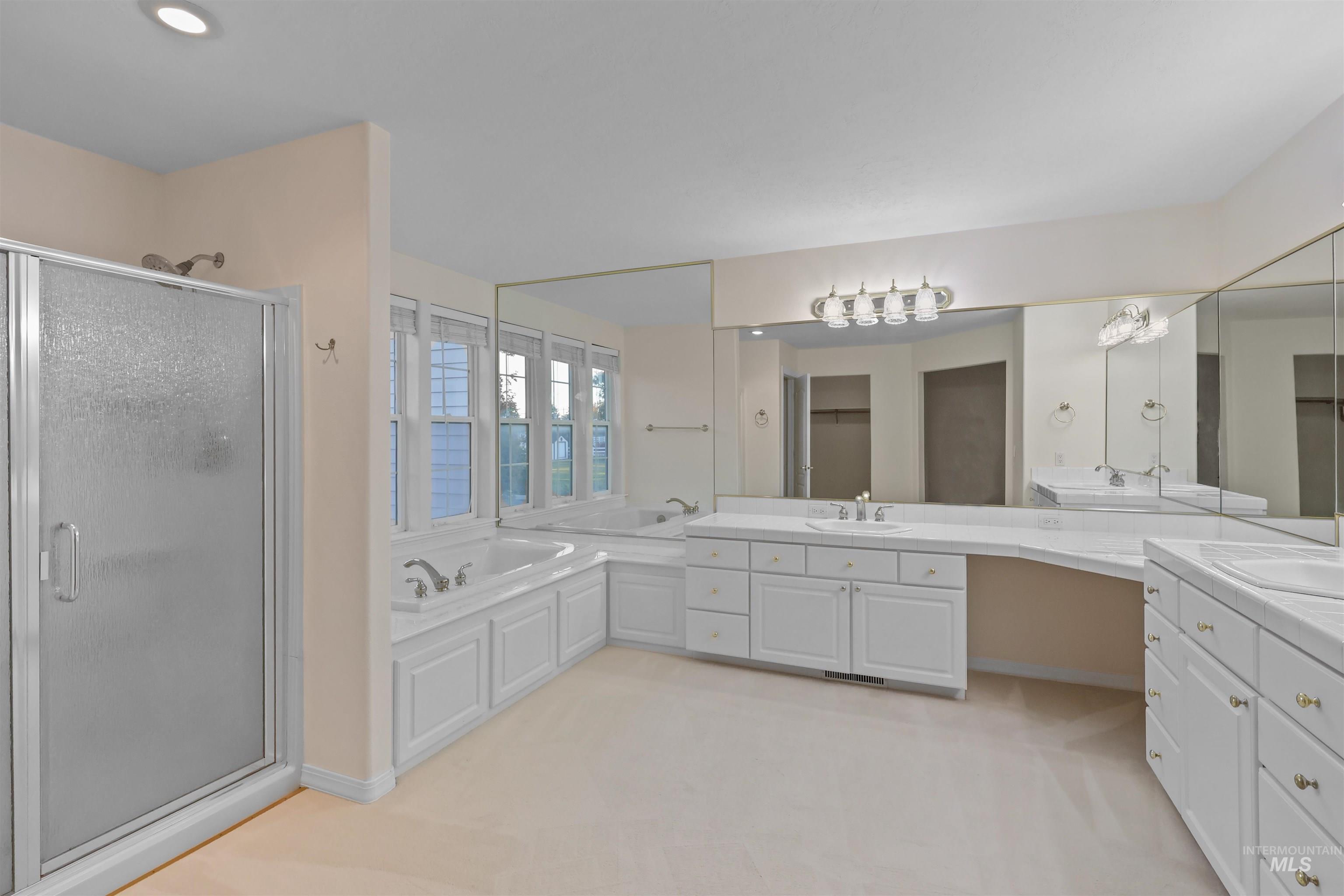 Bathroom with a garden tub, two vanities, a shower stall, and light carpet