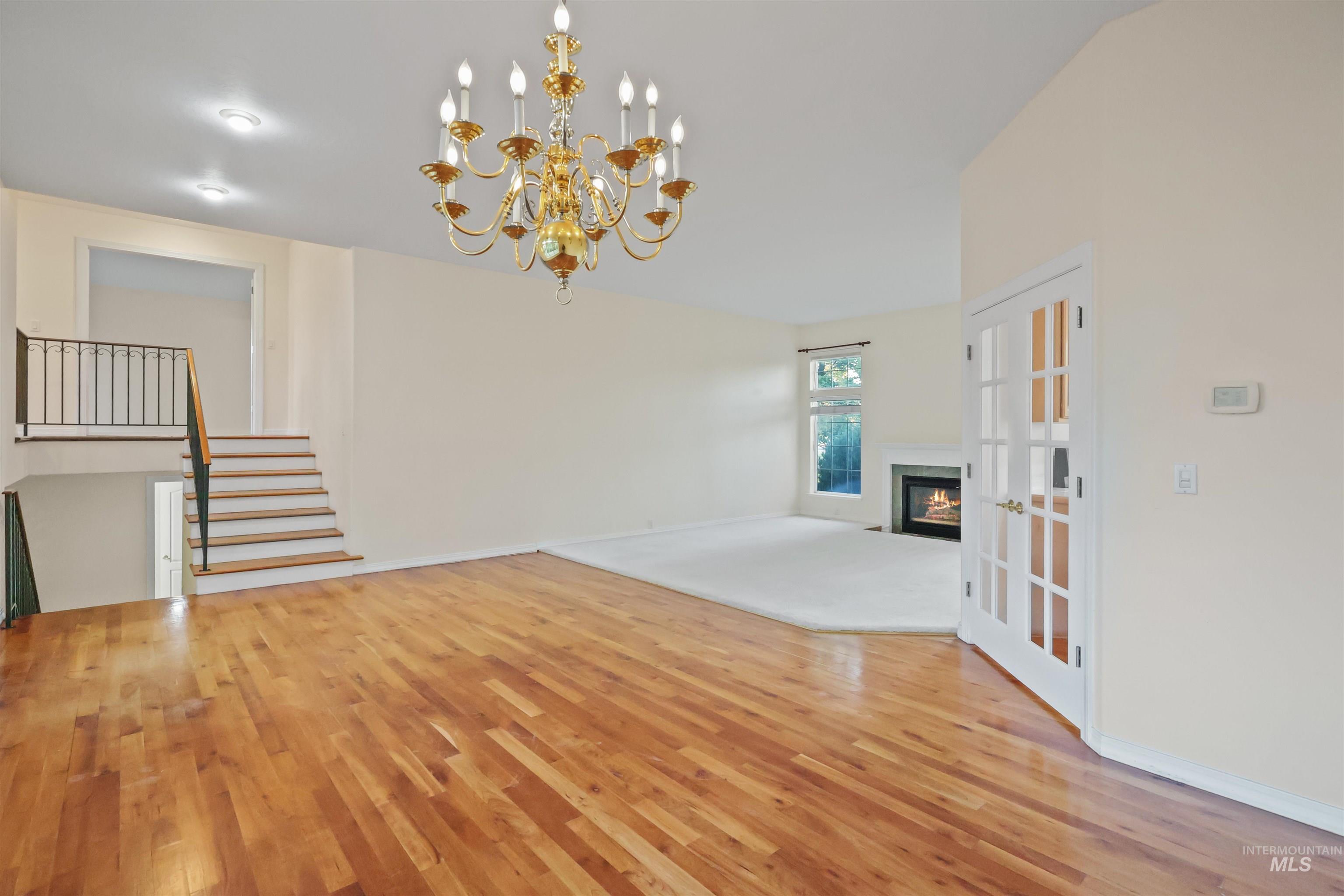 Unfurnished living room with light wood-type flooring, a chandelier, a glass covered fireplace, french doors, and stairs