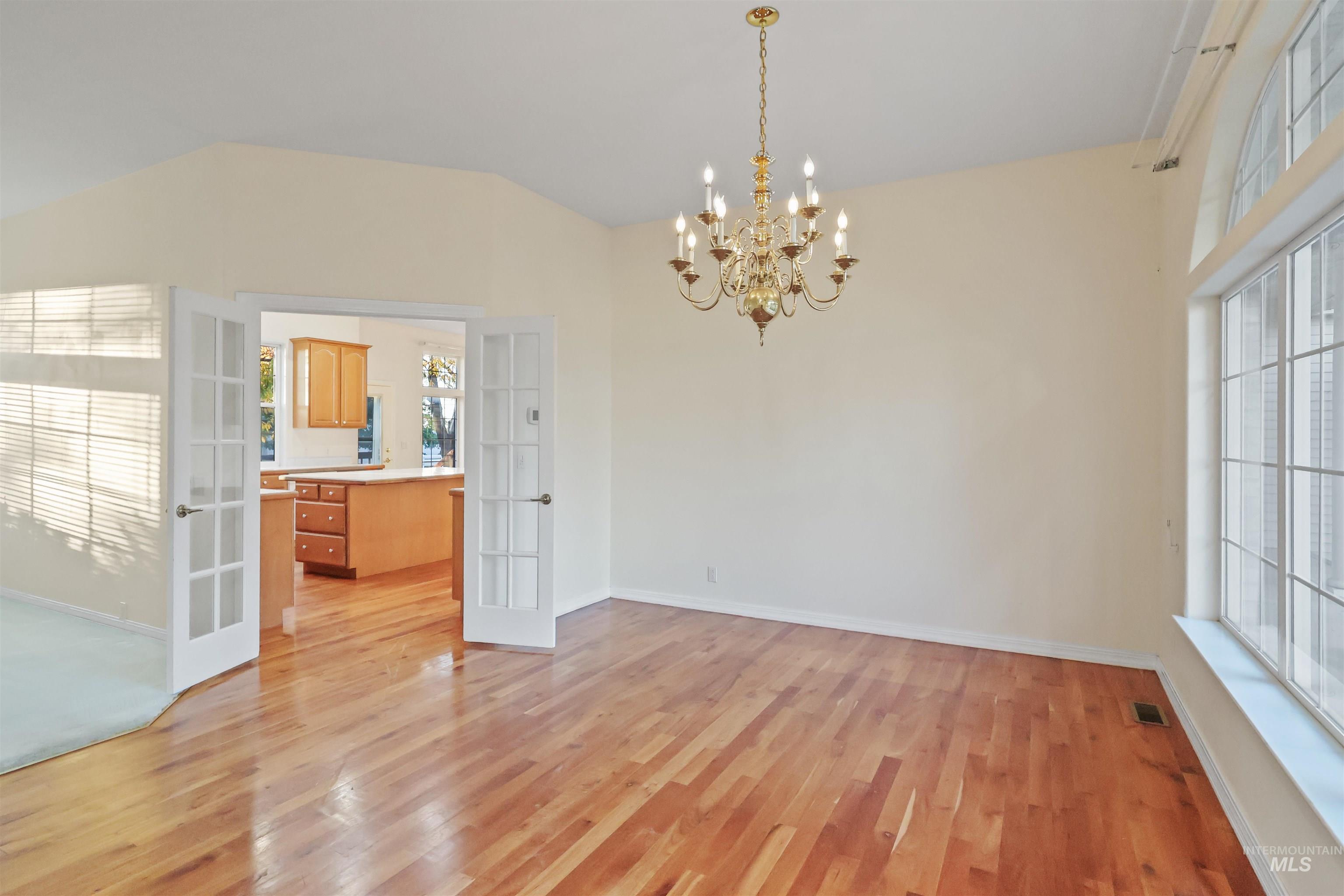 Unfurnished dining area featuring french doors, a chandelier, light wood-style flooring, and lofted ceiling