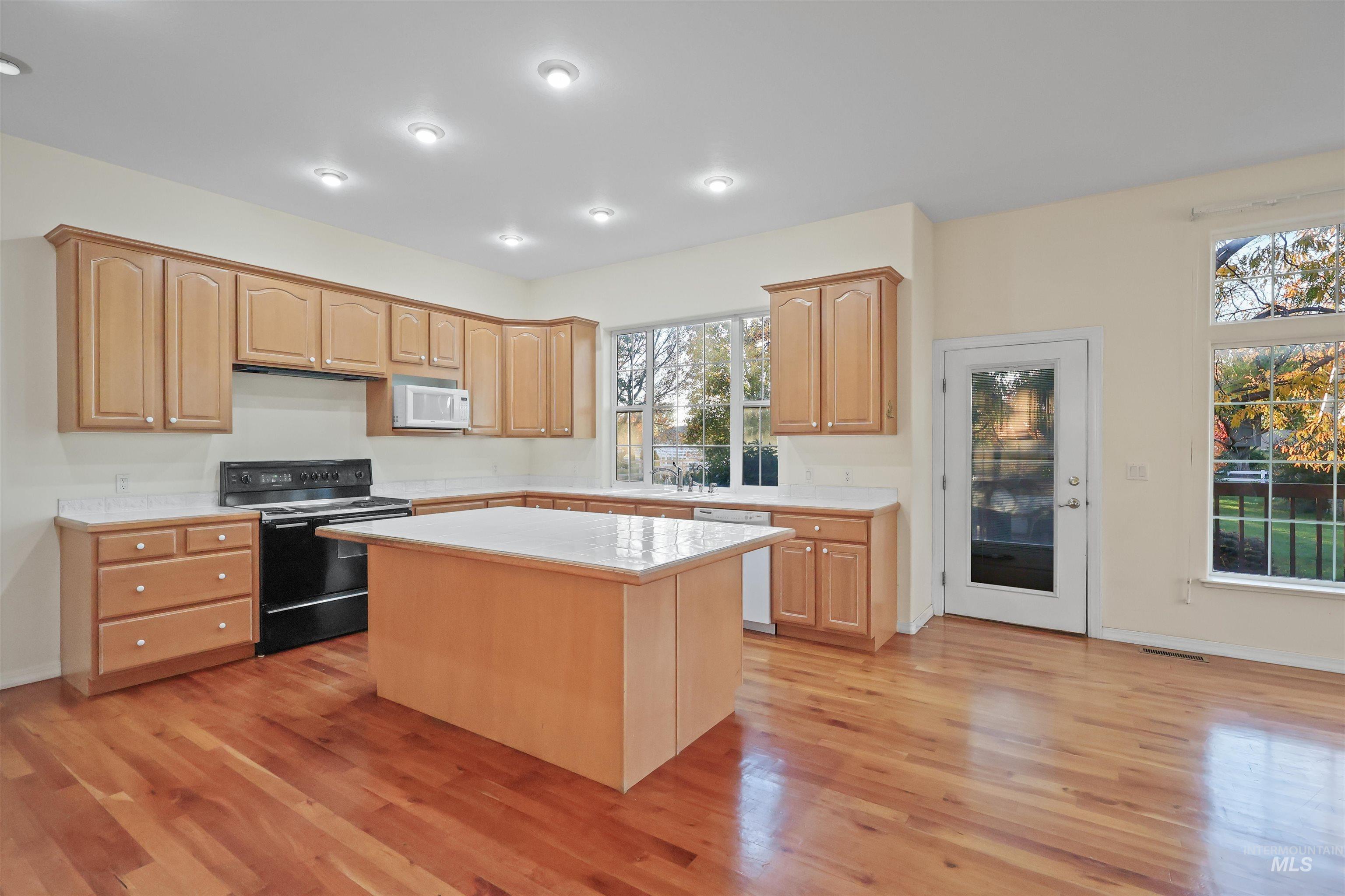 Kitchen featuring white appliances, a center island, light wood finished floors, and light brown cabinets