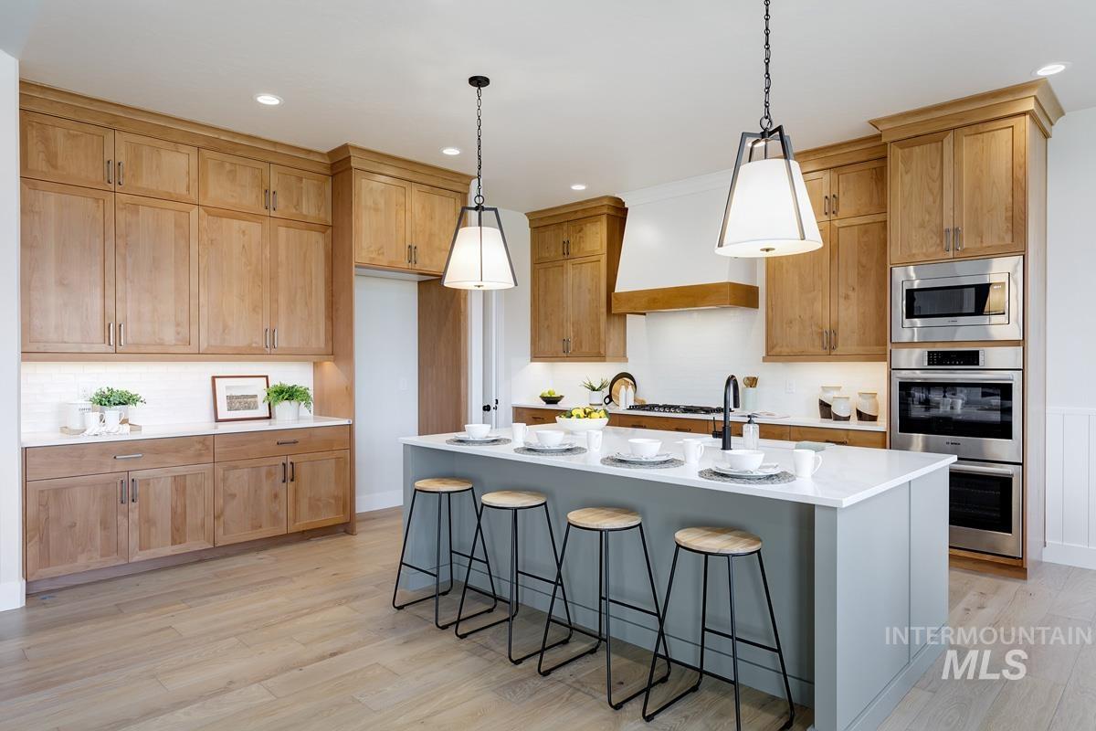 Kitchen featuring a breakfast bar area, an island with sink, stainless steel appliances, light wood-type flooring, and decorative light fixtures