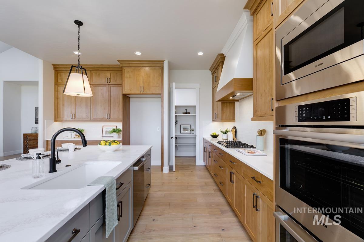 Kitchen featuring hanging light fixtures, stainless steel appliances, light wood-style flooring, recessed lighting, and light stone counters