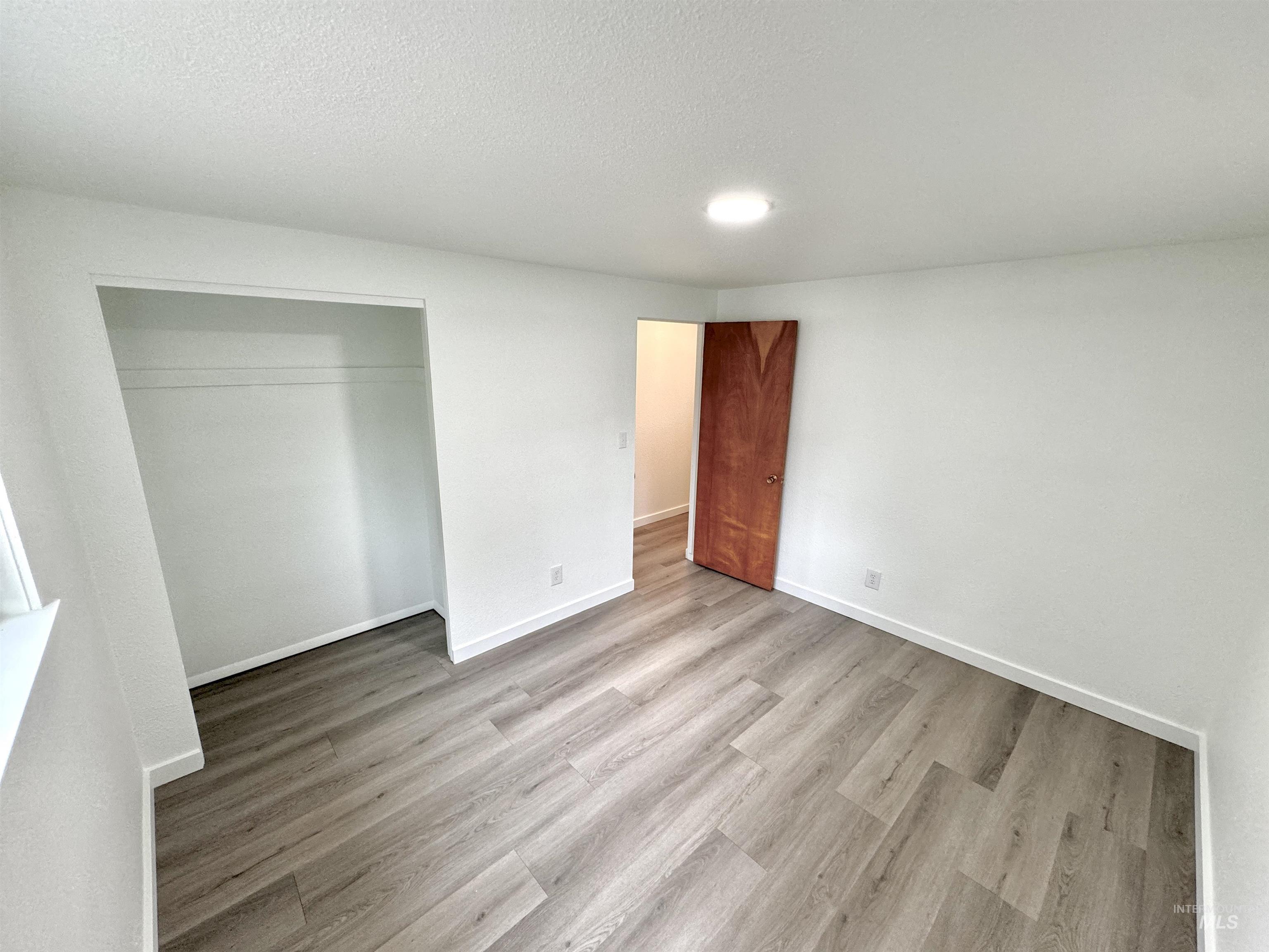 Unfurnished bedroom featuring light wood-type flooring, a textured ceiling, and a closet