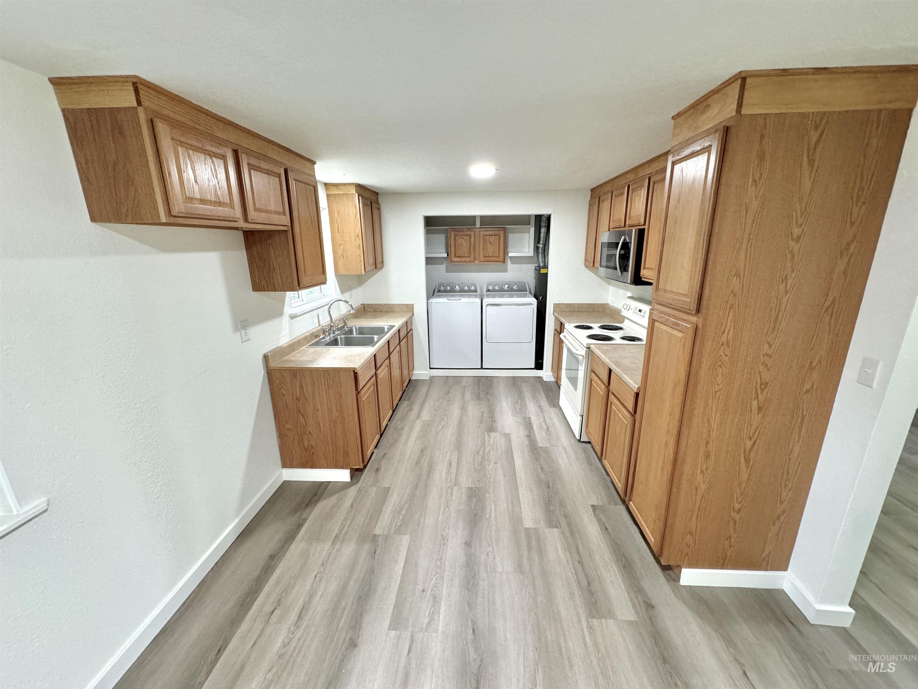 Kitchen featuring washing machine and clothes dryer, white electric stove, light countertops, light wood finished floors, and brown cabinetry
