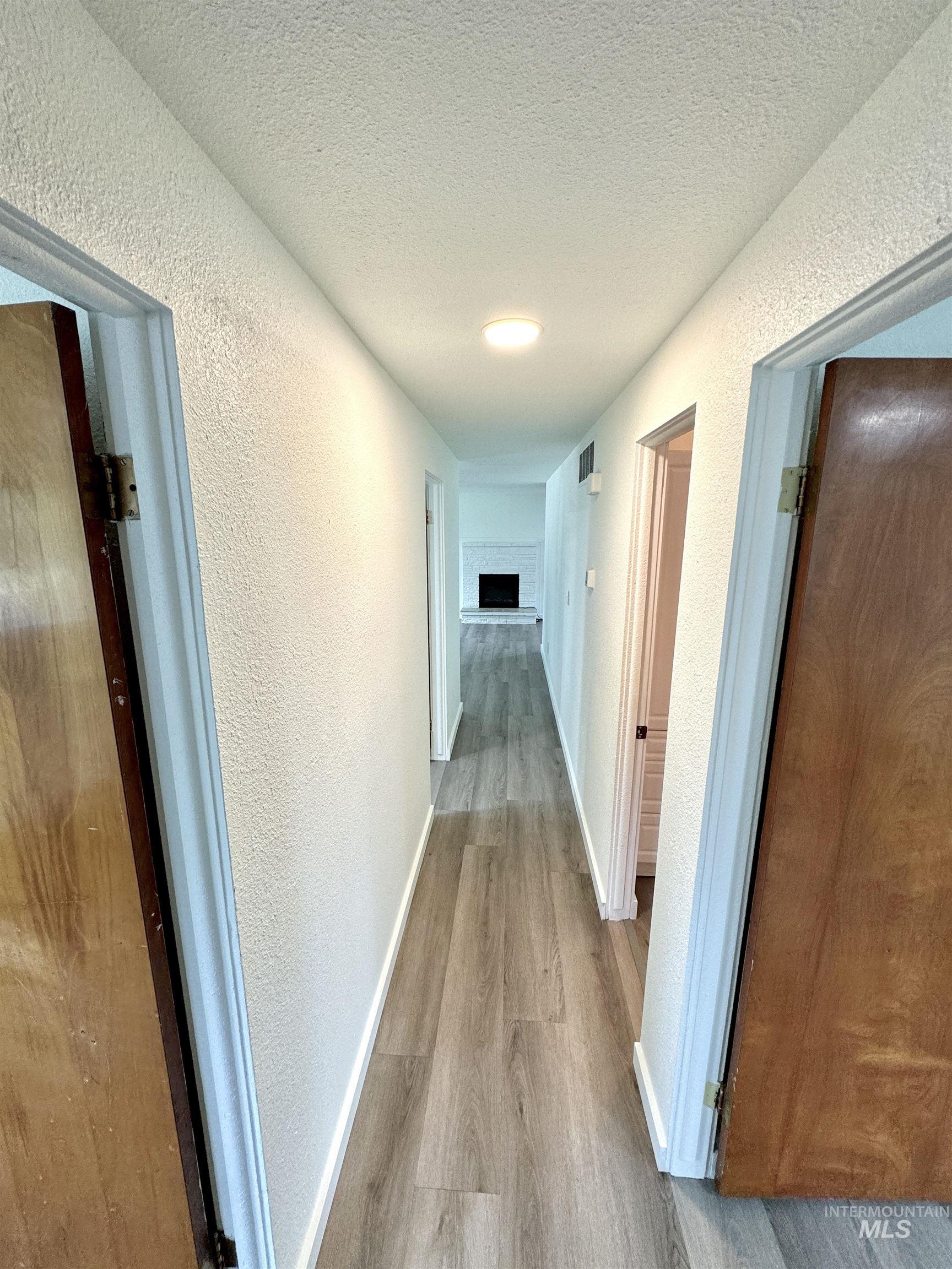 Corridor with light wood-style flooring, a textured wall, and a textured ceiling