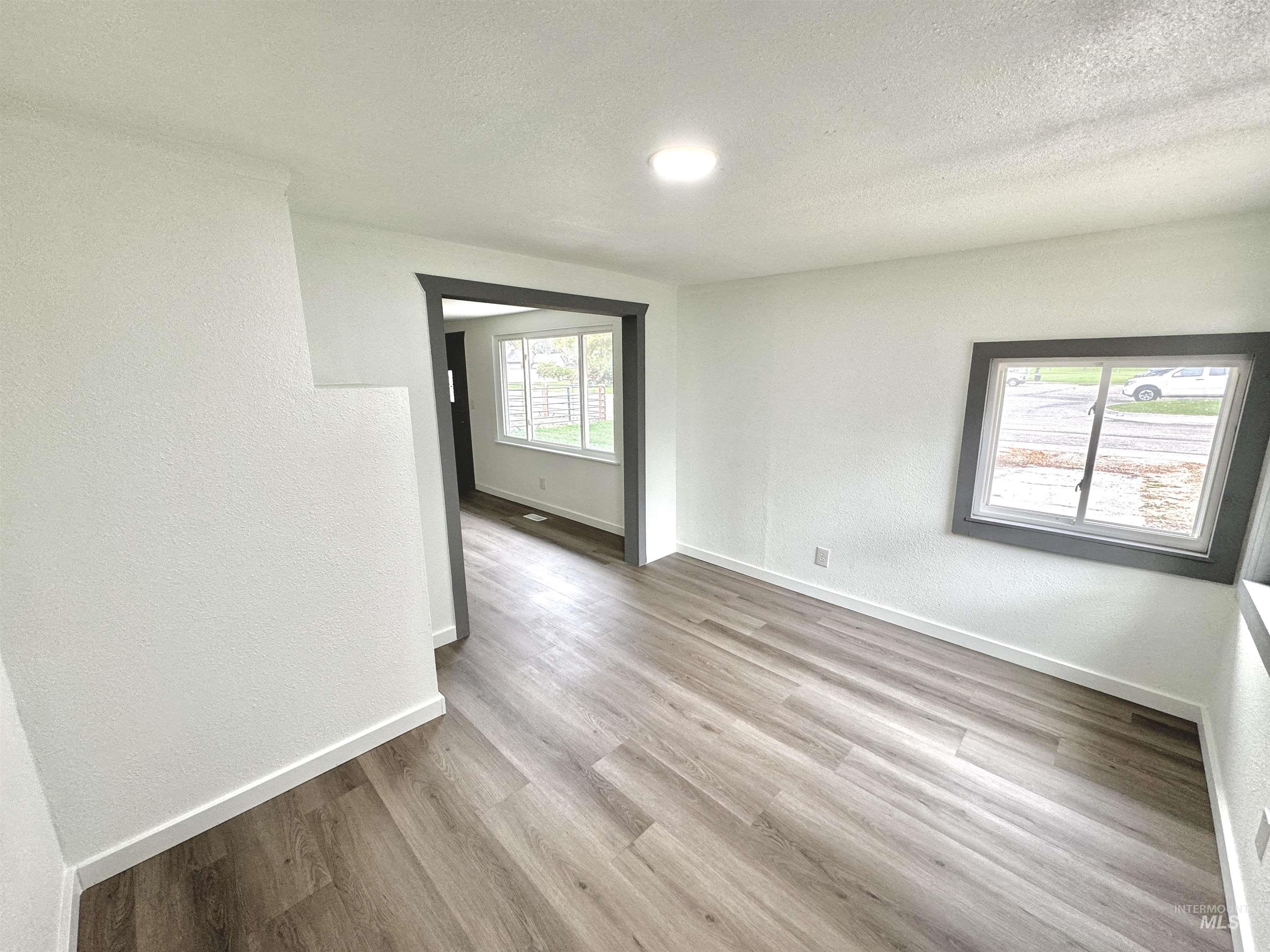 Empty room featuring a textured wall, light wood-style flooring, and a textured ceiling