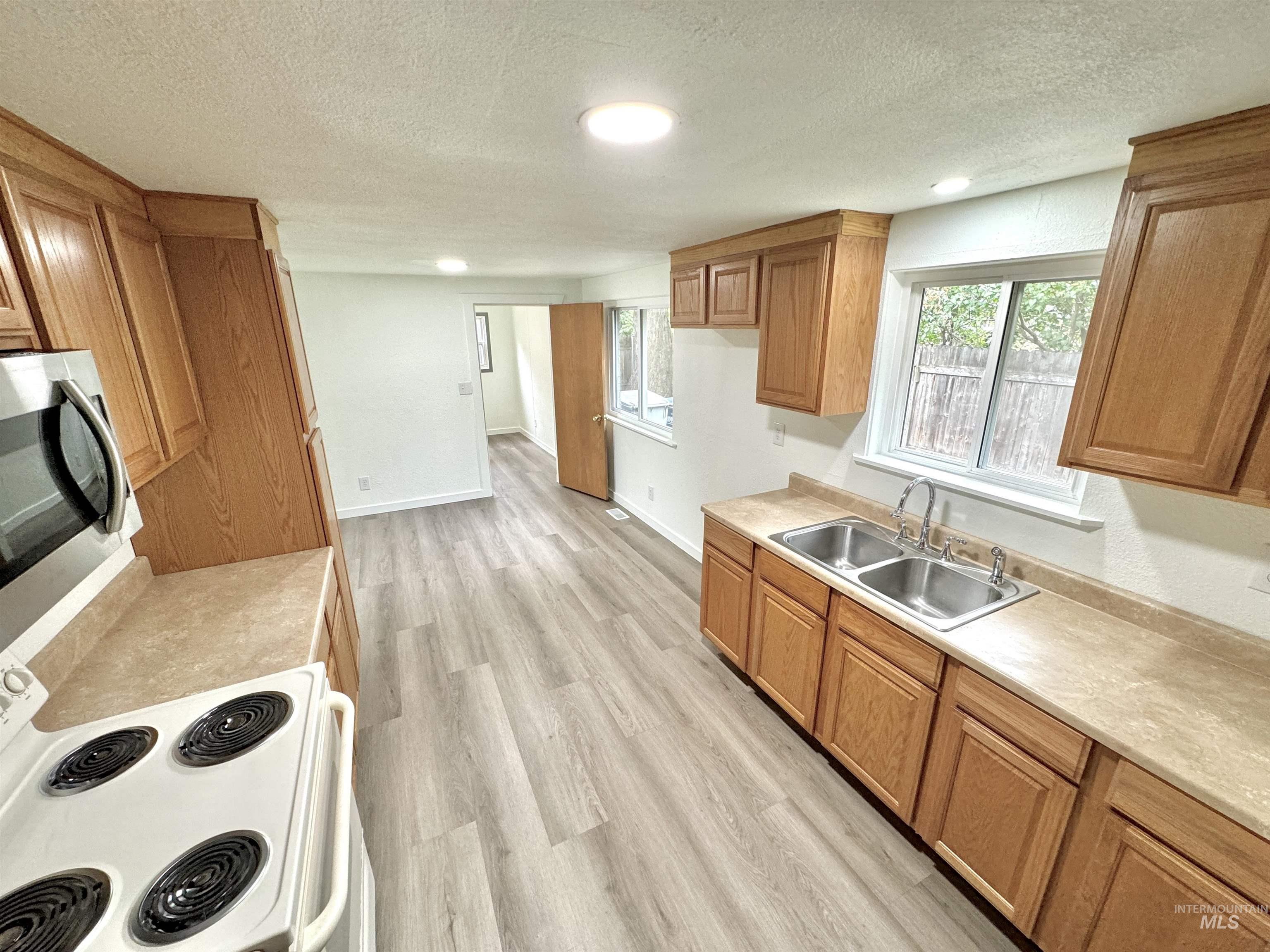 Kitchen with white electric range, brown cabinets, light countertops, a textured ceiling, and light wood finished floors