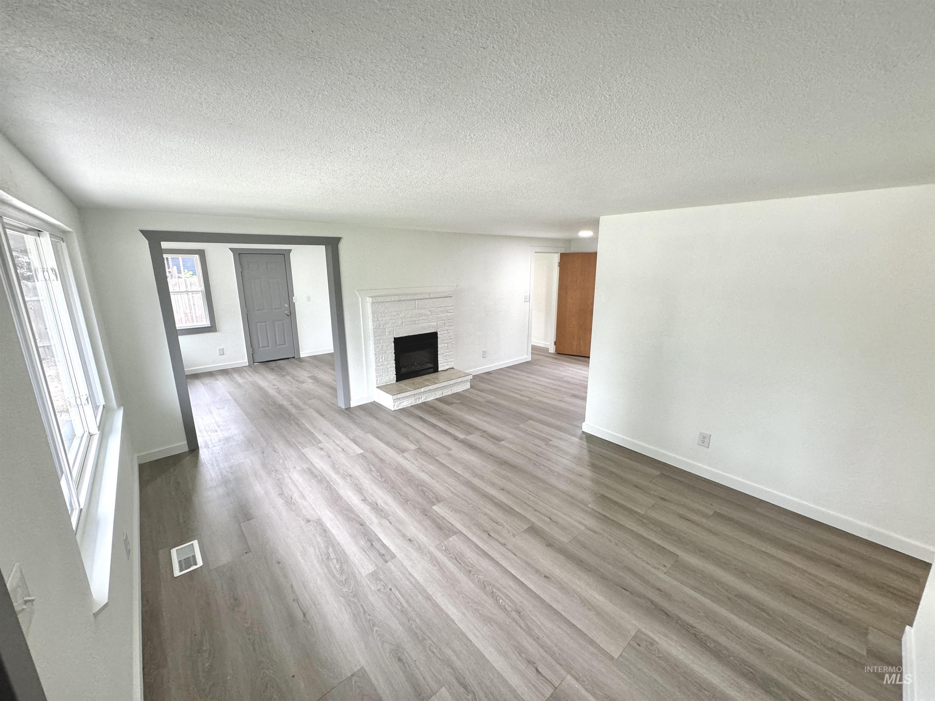 Unfurnished living room with a textured ceiling, wood finished floors, and a fireplace with raised hearth