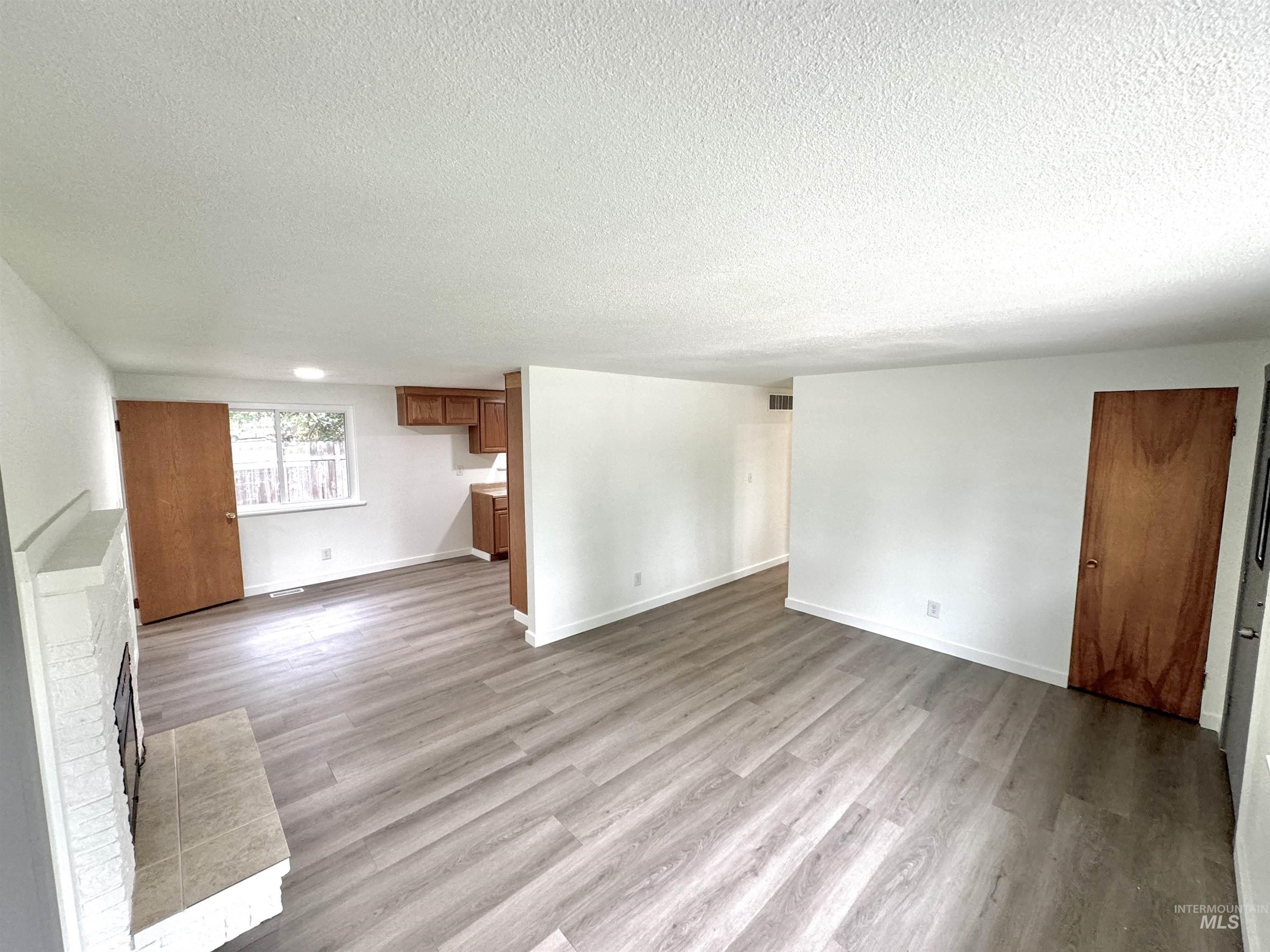 Unfurnished living room with a fireplace, light wood-type flooring, and a textured ceiling