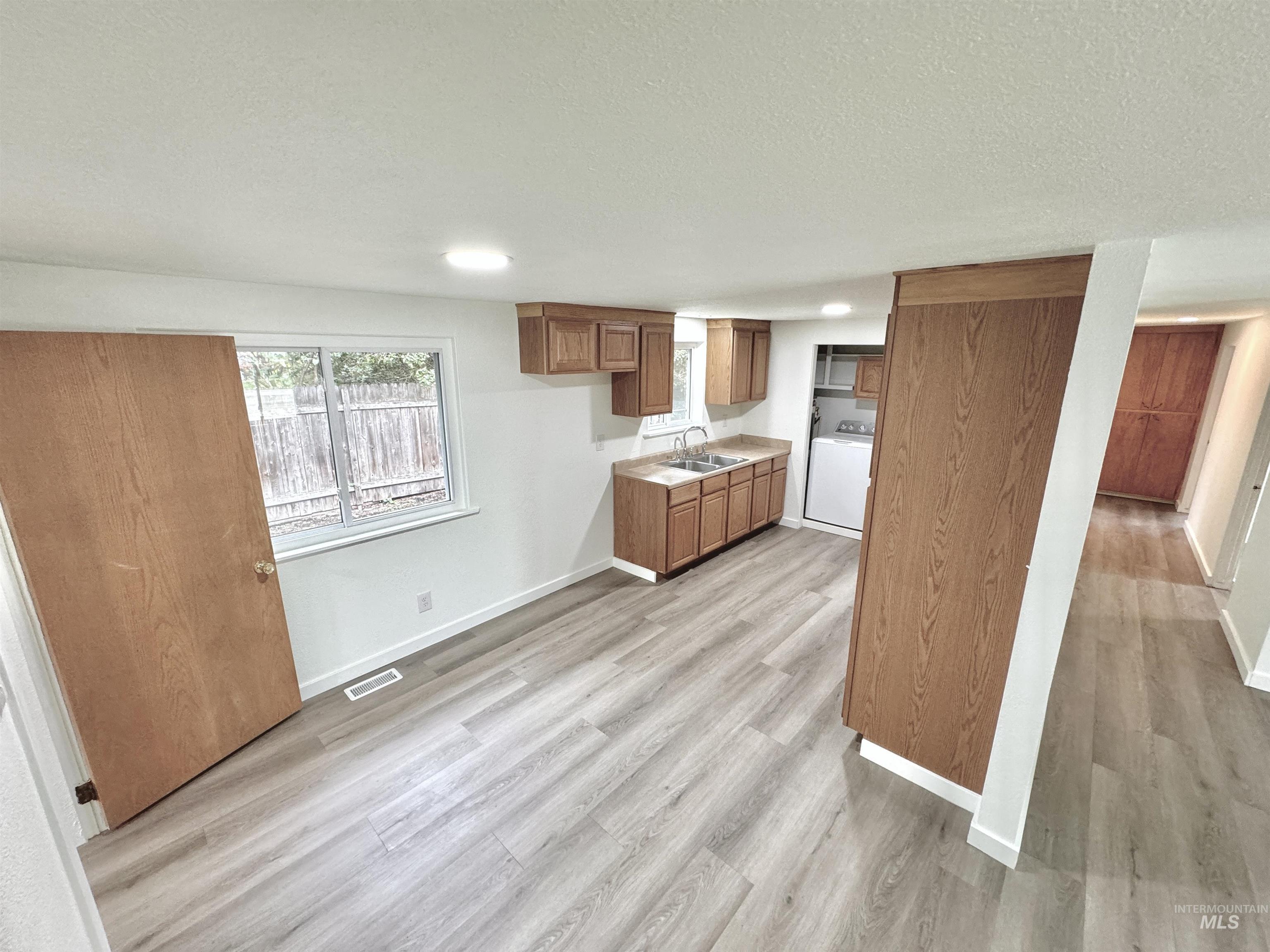 Kitchen with brown cabinetry, light countertops, light wood finished floors, recessed lighting, and washer / clothes dryer