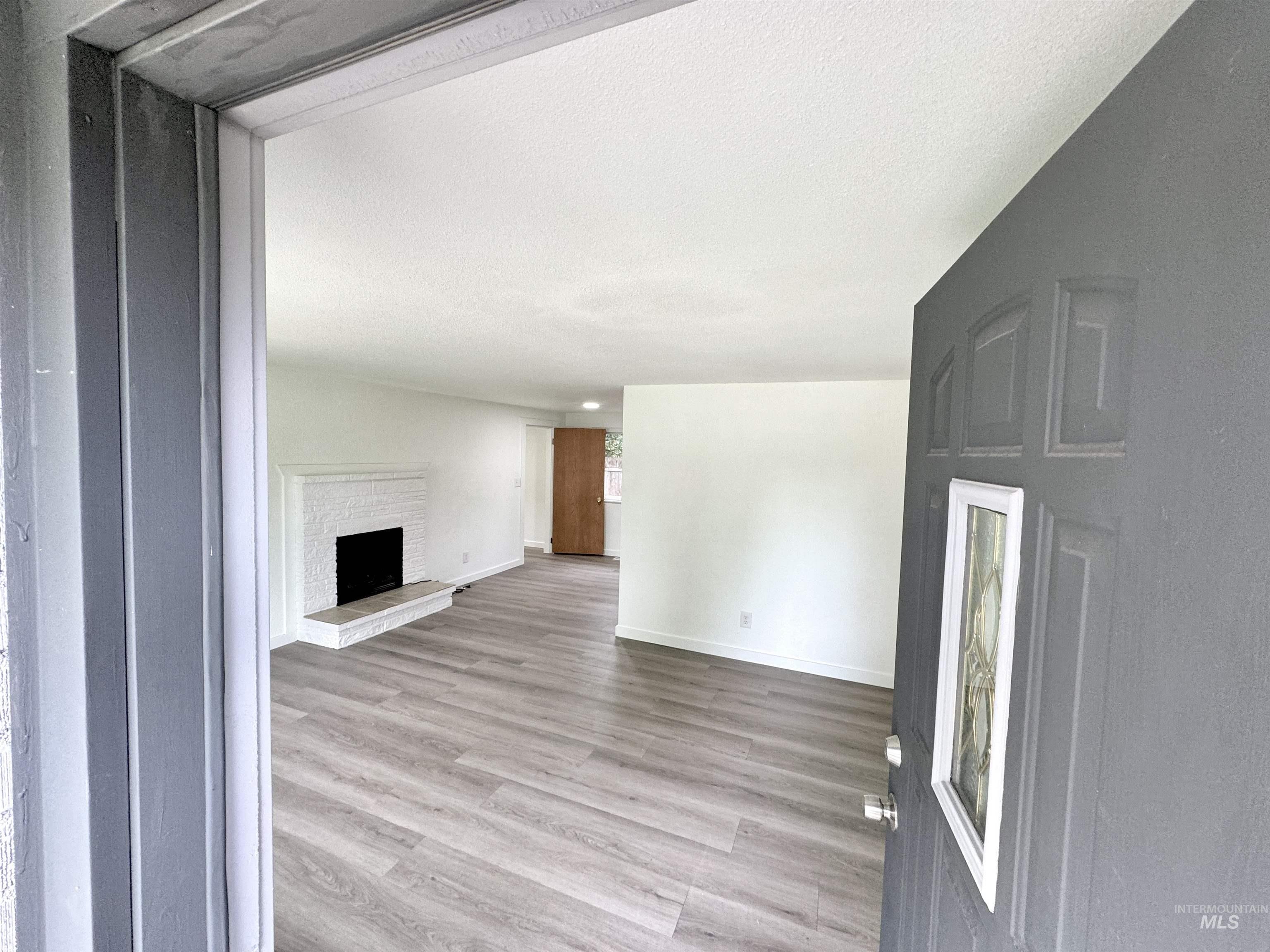 Unfurnished living room featuring light wood-type flooring, a brick fireplace, and a textured ceiling