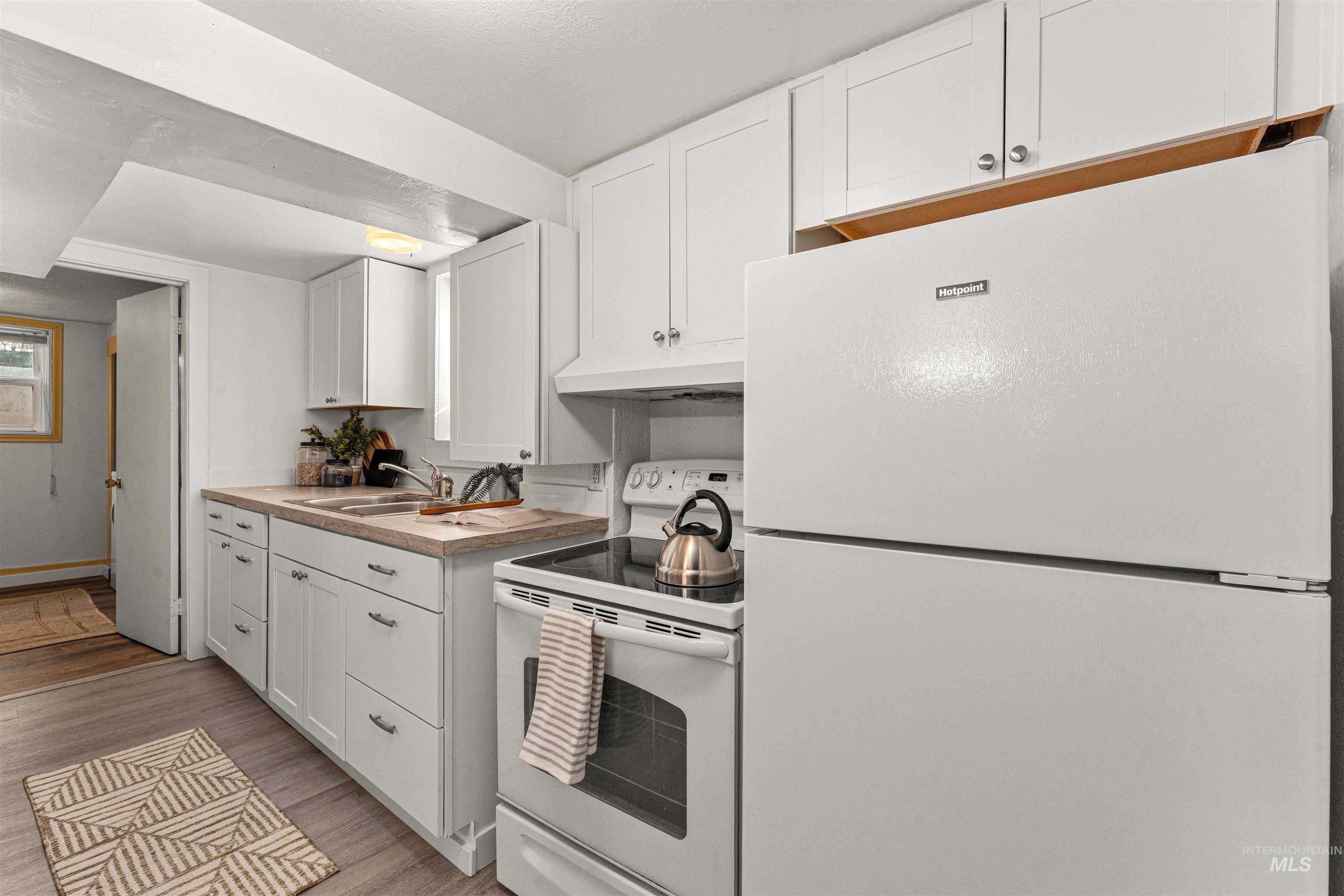 Kitchen featuring white appliances, white cabinetry, light wood-type flooring, light countertops, and a textured ceiling
