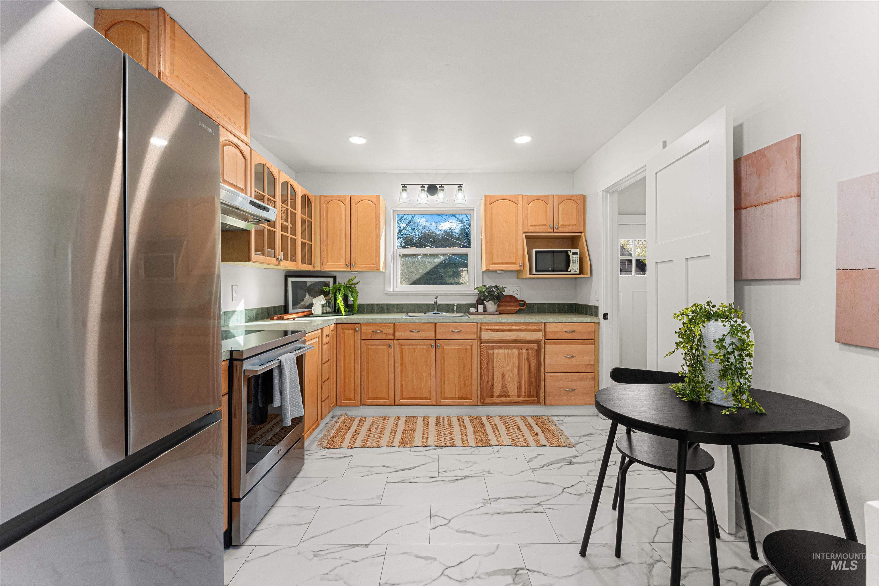 Kitchen with stainless steel appliances, glass insert cabinets, light marble finish flooring, light countertops, and recessed lighting