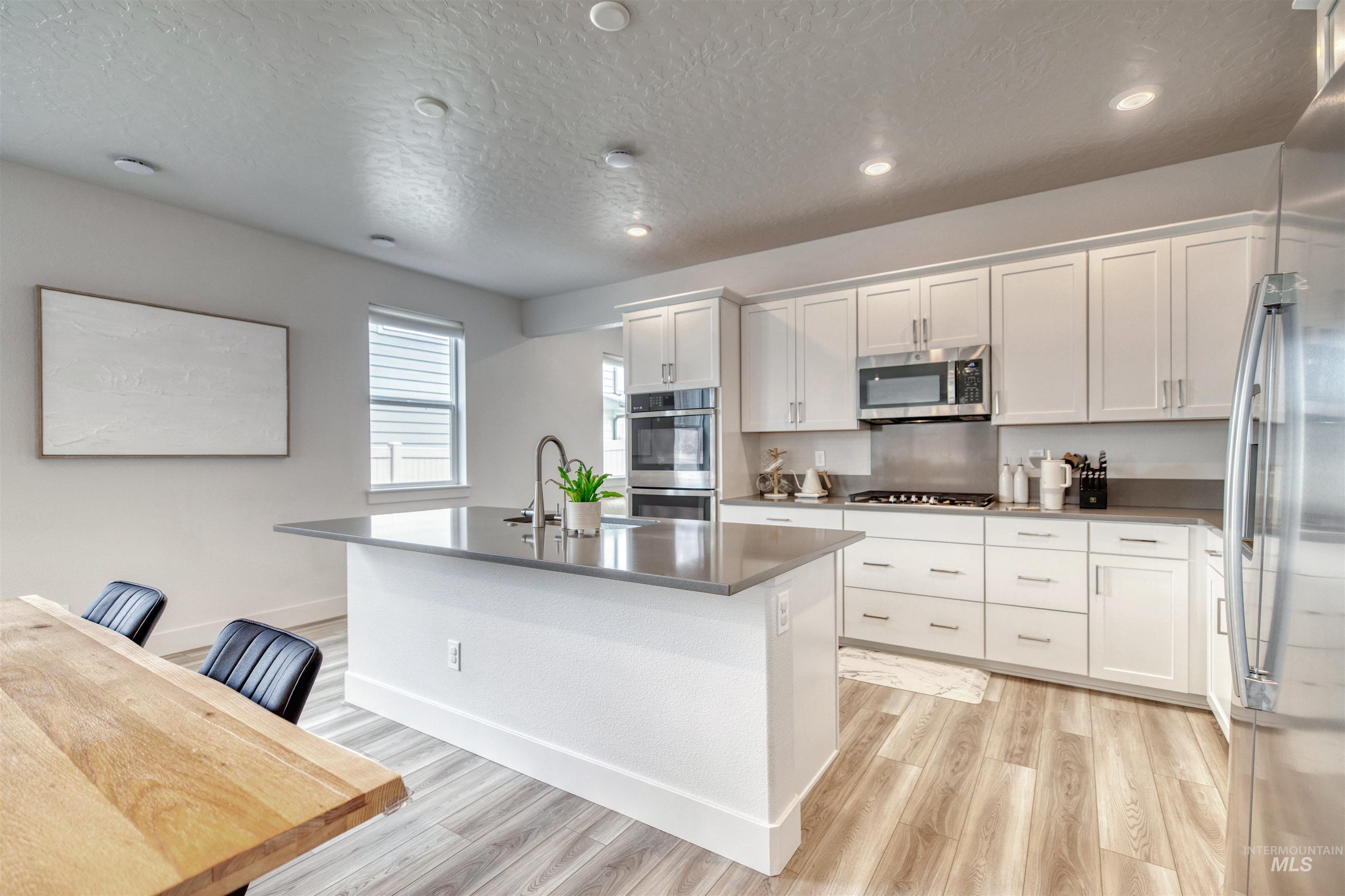 Kitchen featuring a kitchen island with sink, white cabinetry, light wood-style floors, appliances with stainless steel finishes, and a textured ceiling