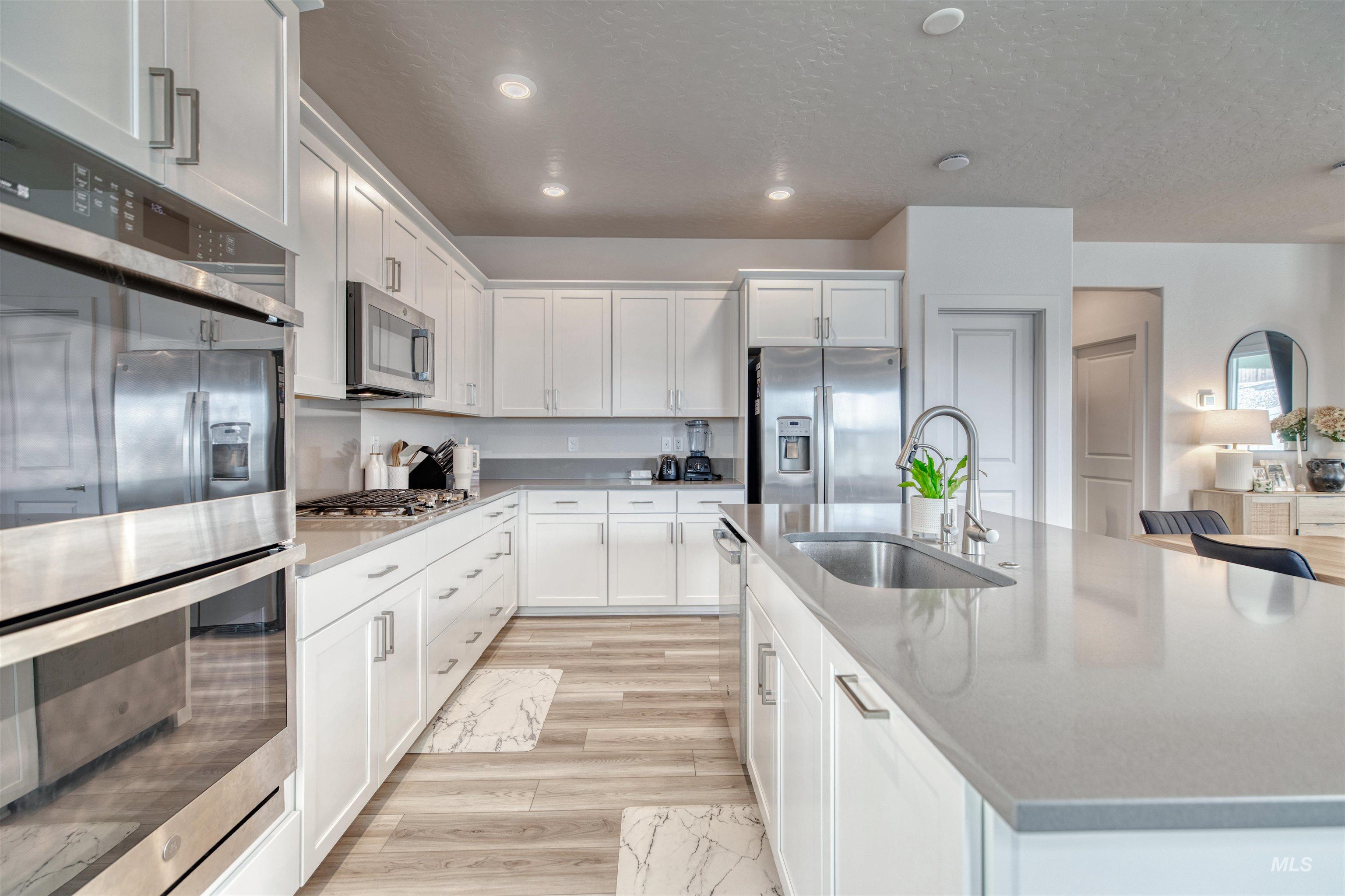 Kitchen with appliances with stainless steel finishes, white cabinets, light stone counters, a center island with sink, and light wood-type flooring