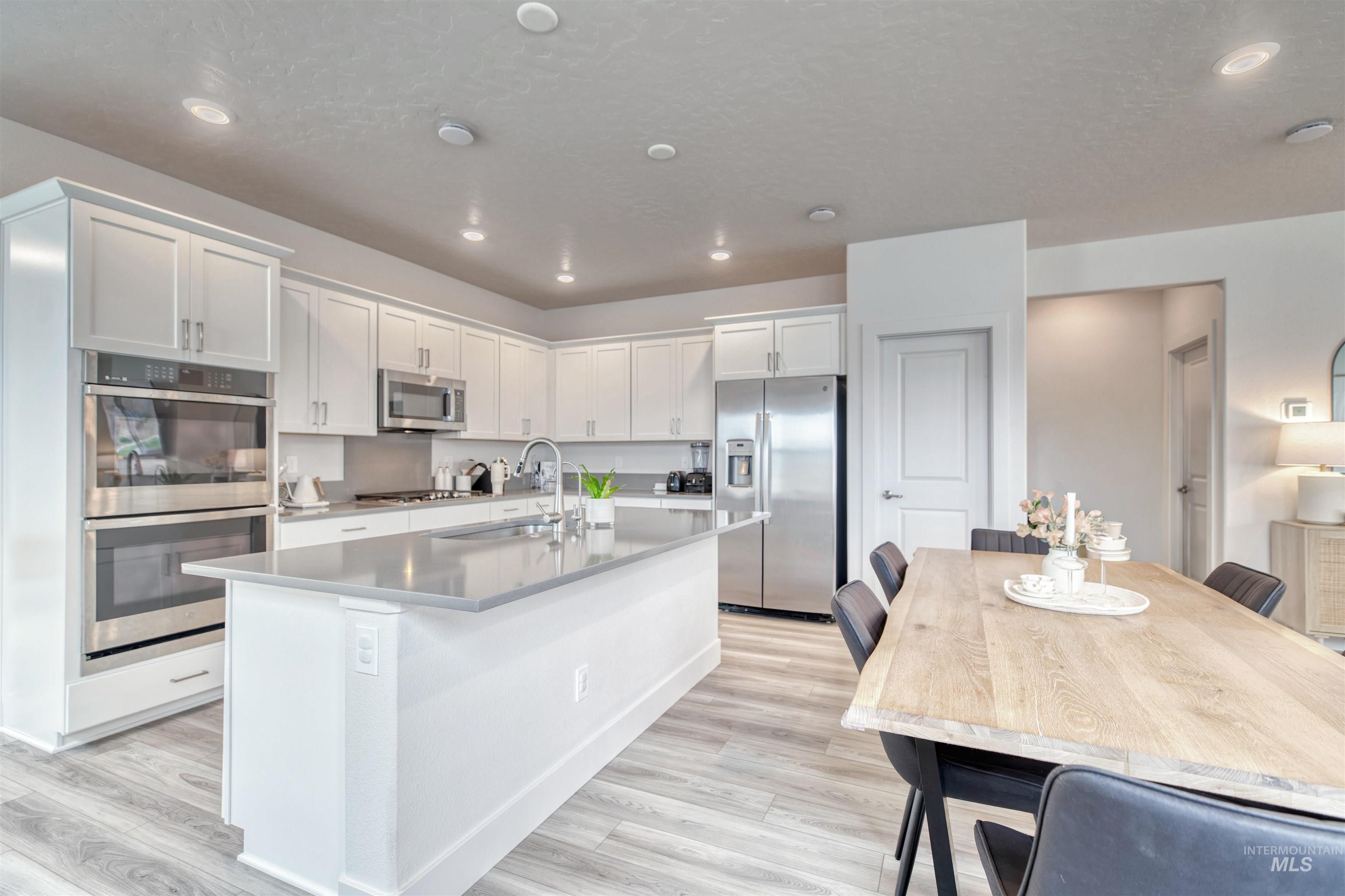 Kitchen with white cabinets, stainless steel appliances, light wood-style floors, recessed lighting, and an island with sink