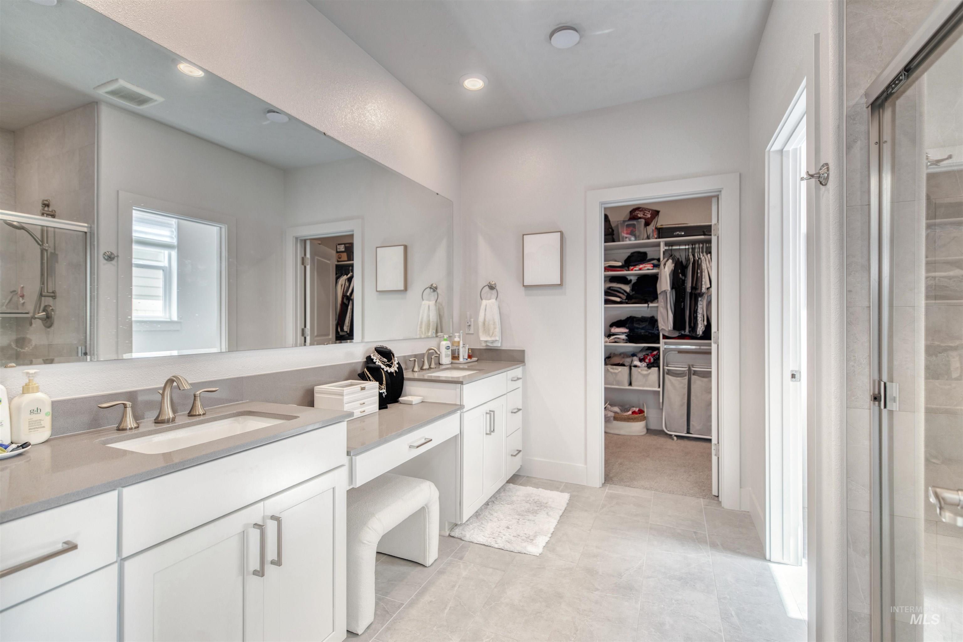 Bathroom featuring a walk in closet, a stall shower, double vanity, and recessed lighting