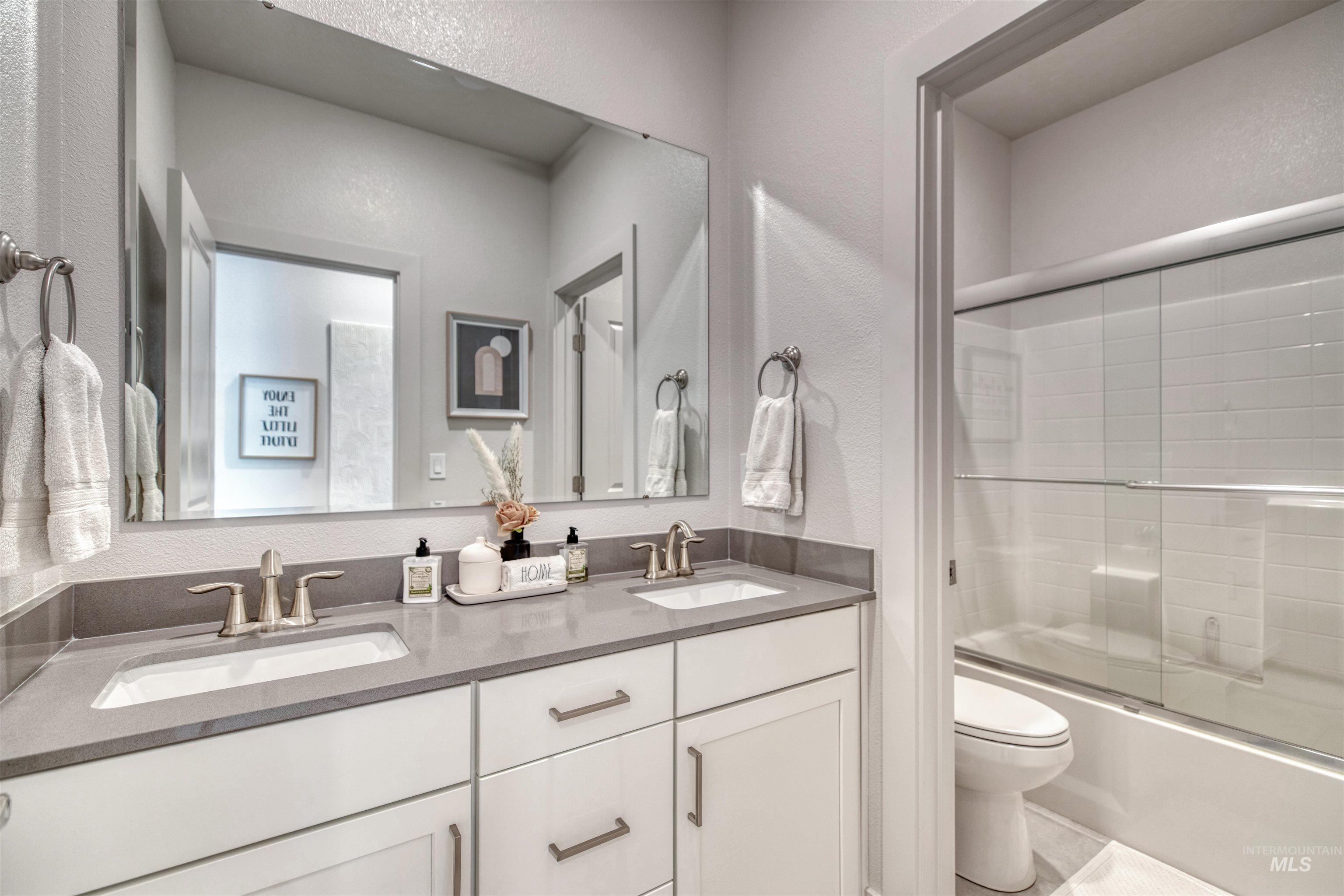 Full bathroom with a textured wall, combined bath / shower with glass door, and double vanity