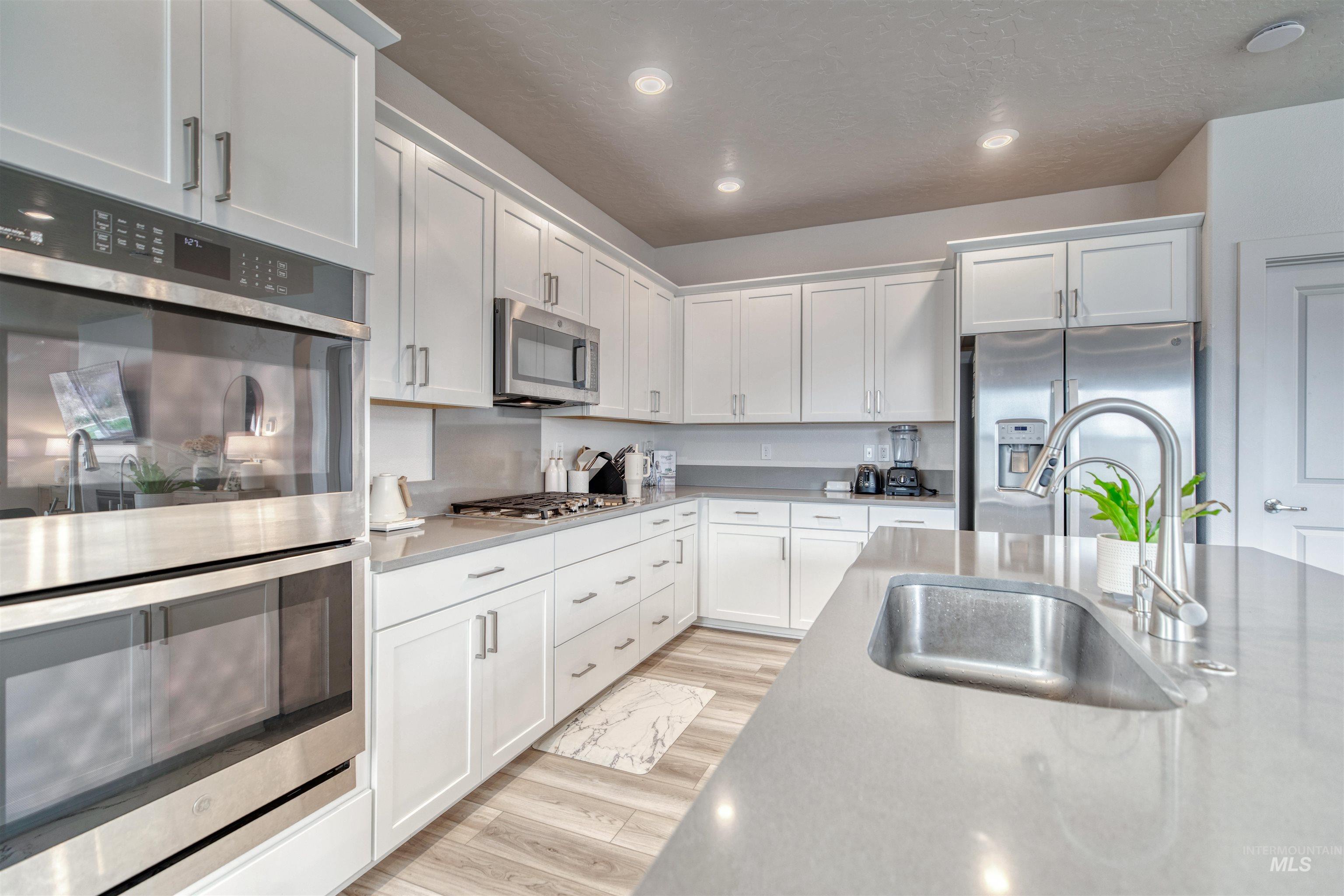 Kitchen featuring stainless steel appliances, white cabinets, light wood-type flooring, recessed lighting, and light stone countertops