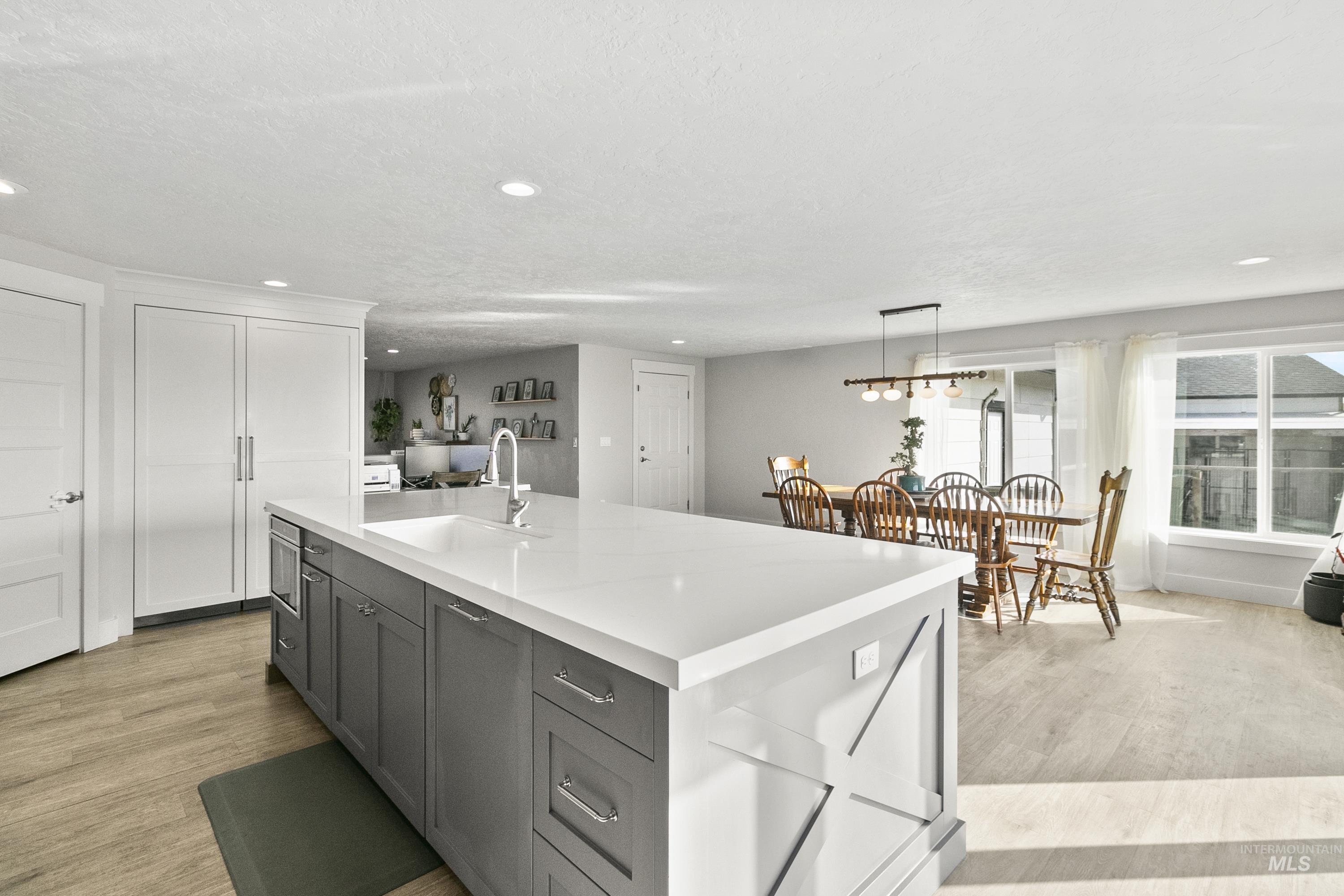Kitchen featuring pendant lighting, gray cabinets, light wood finished floors, a kitchen island with sink, and recessed lighting