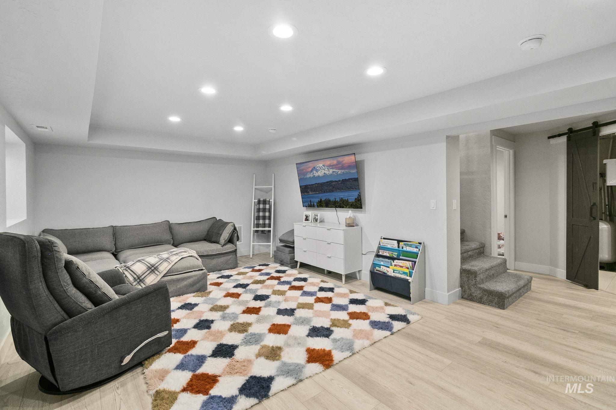 Living area featuring a barn door, recessed lighting, light wood-style flooring, a raised ceiling, and stairway