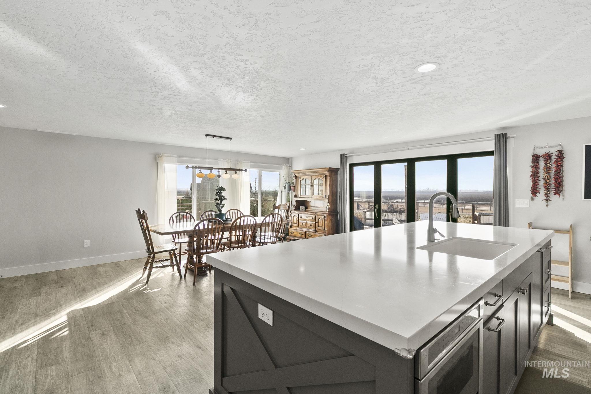 Kitchen with light countertops, light wood-style floors, decorative light fixtures, a kitchen island with sink, and a textured ceiling