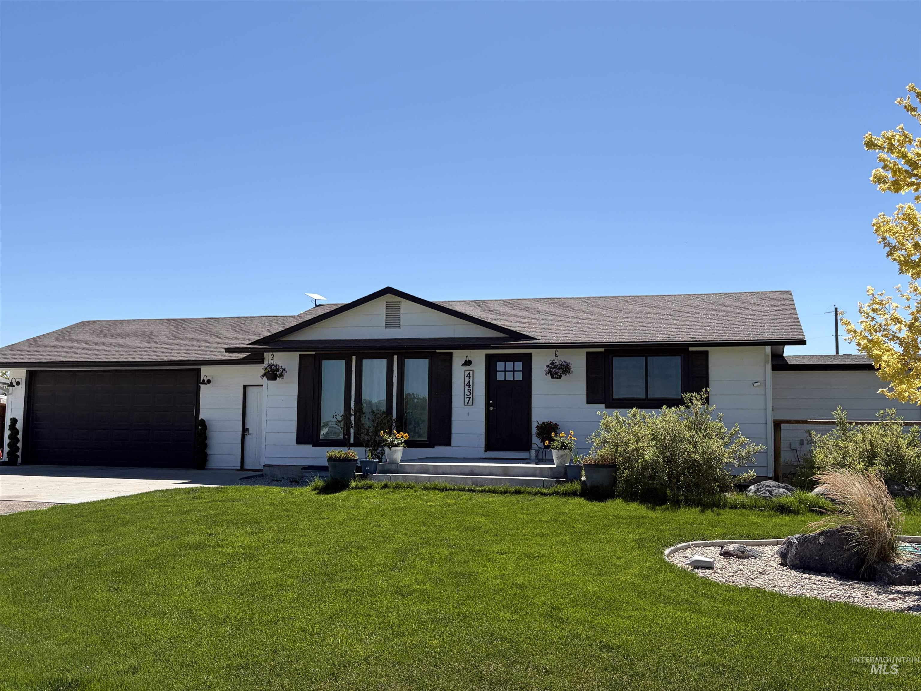 White exterior with black trim, dark gray garage door, and a brown shingle roof