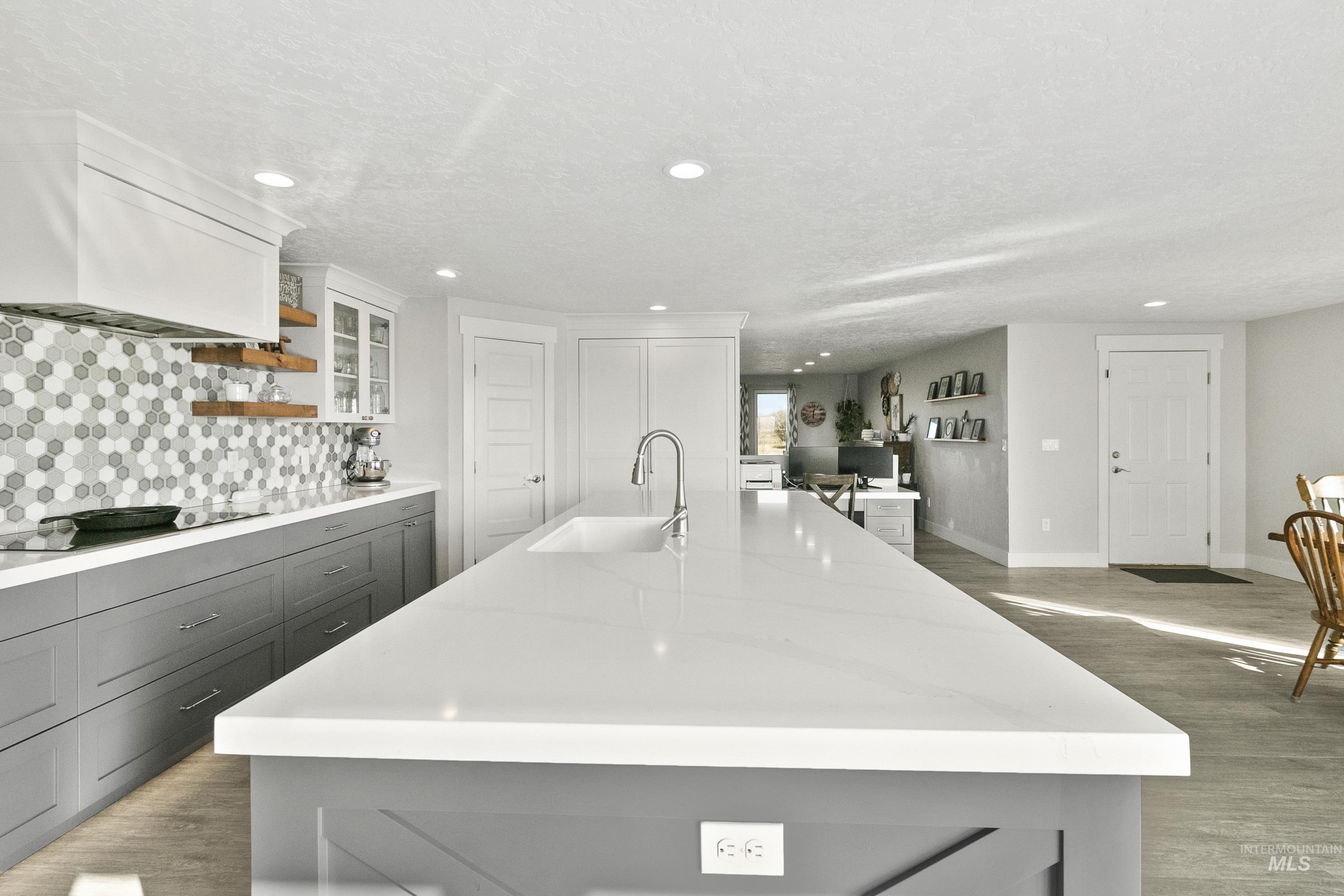 Kitchen with open shelves, a kitchen island with sink, light wood-style floors, glass insert cabinets, and light stone countertops
