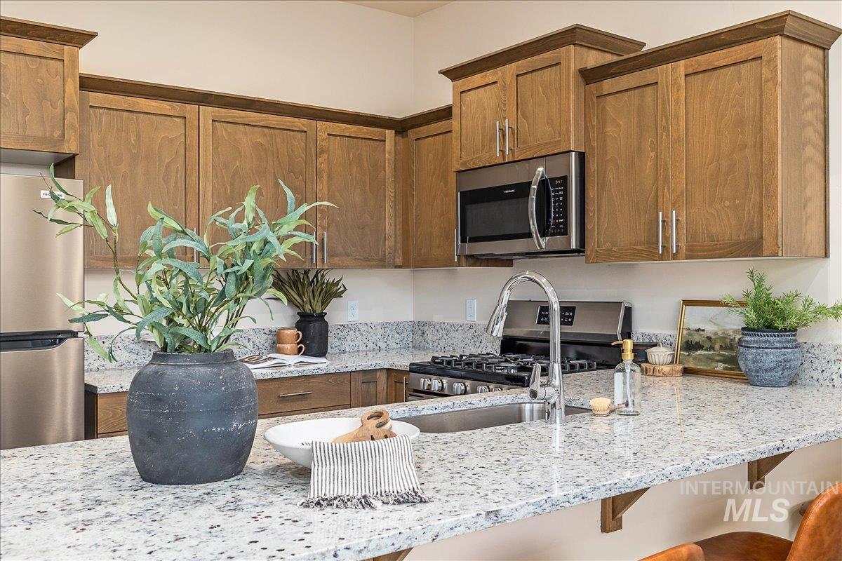Kitchen with stainless steel appliances, light stone counters, brown cabinets, and a breakfast bar area